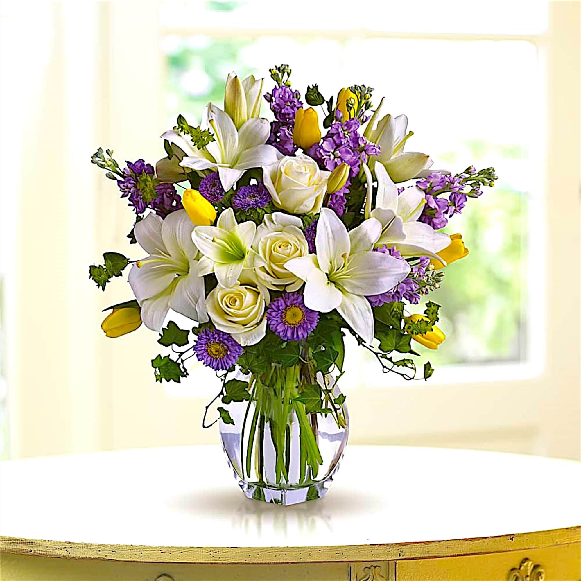 Bouquet of white lilies, yellow tulips, purple flowers, and white roses in a glass vase