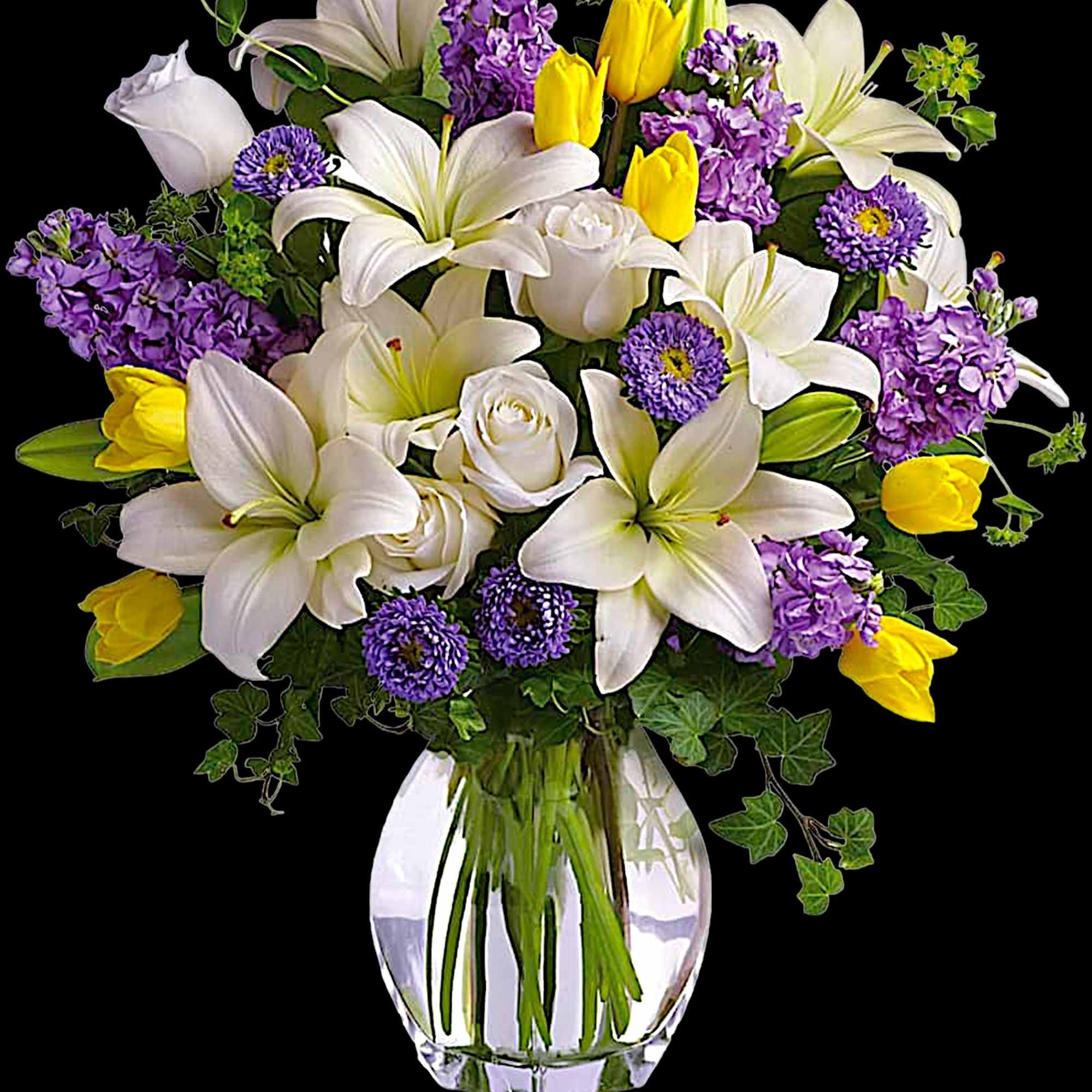 Bouquet of white lilies, purple flowers, and yellow tulips in a clear glass vase