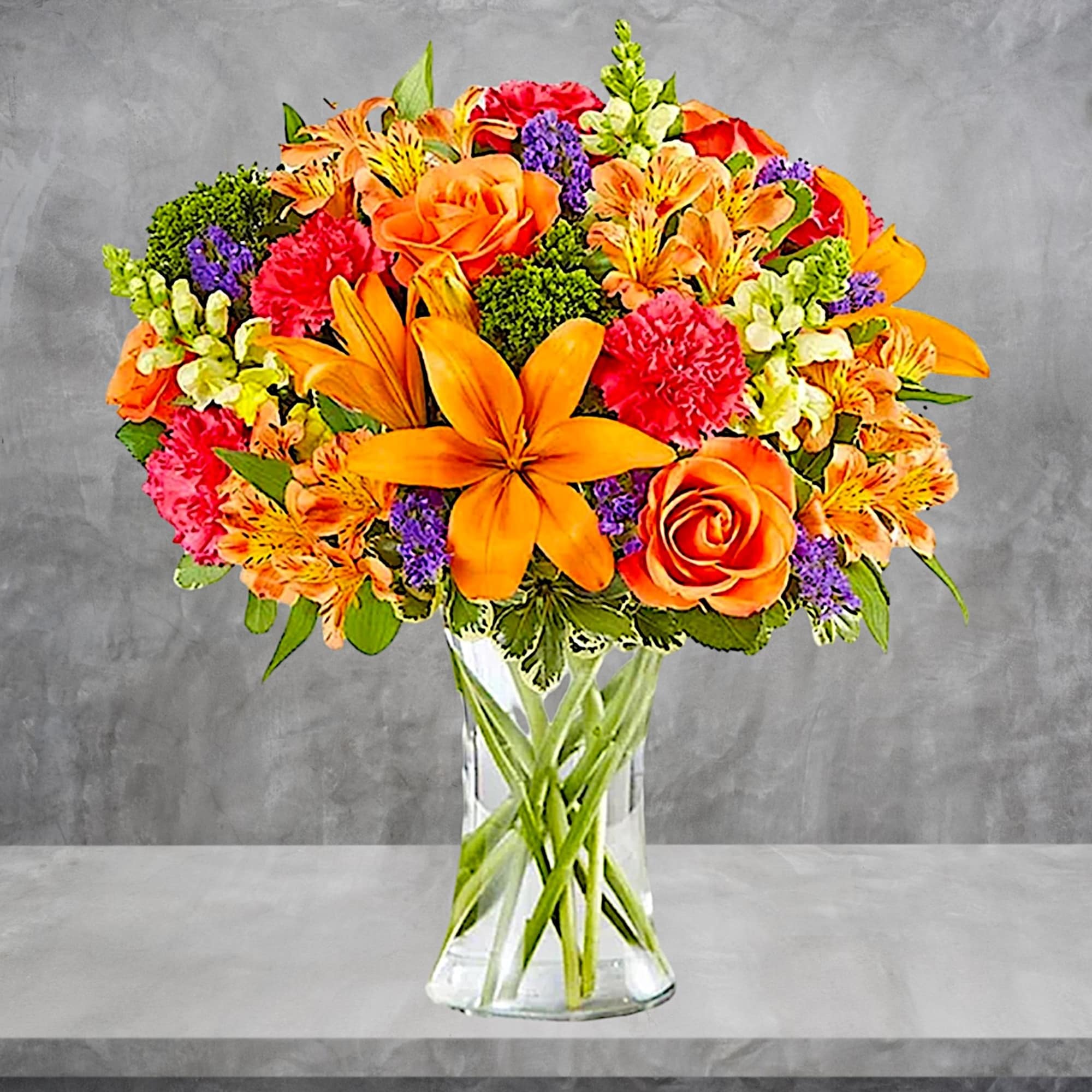 Bright mixed bouquet of orange, pink, purple, and white flowers in a clear vase