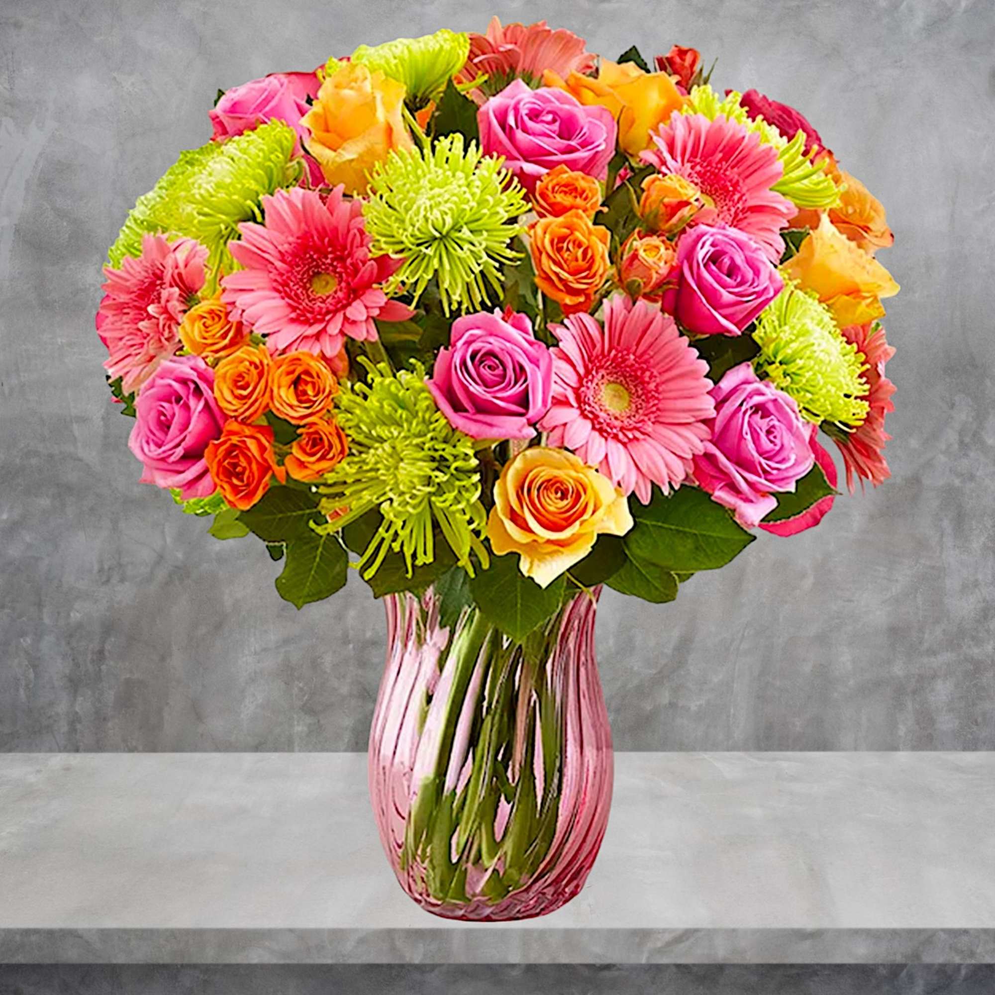 Bright mixed bouquet of roses and gerbera daisies in a pink glass vase