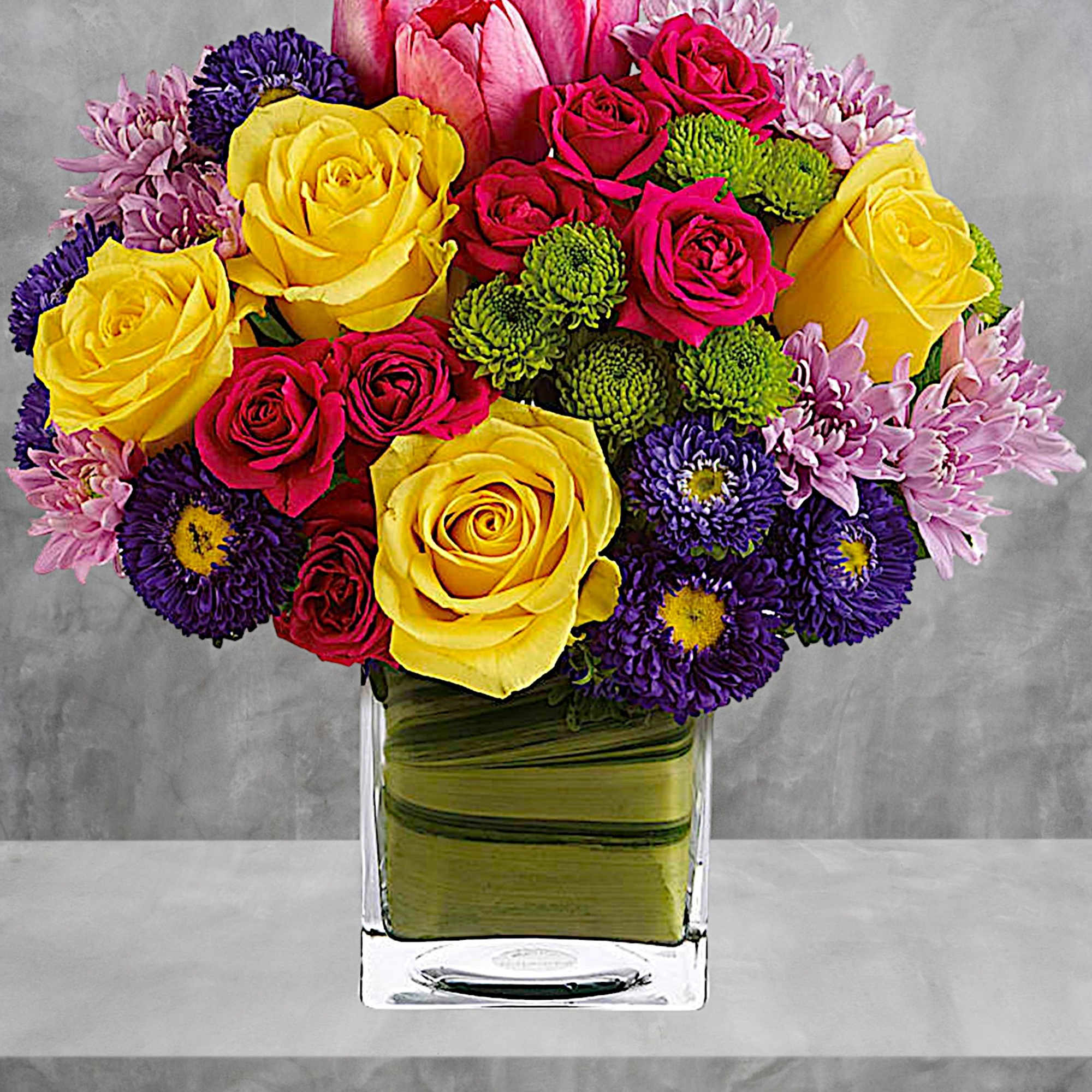 Colorful bouquet of roses, tulips, and mums in a glass vase