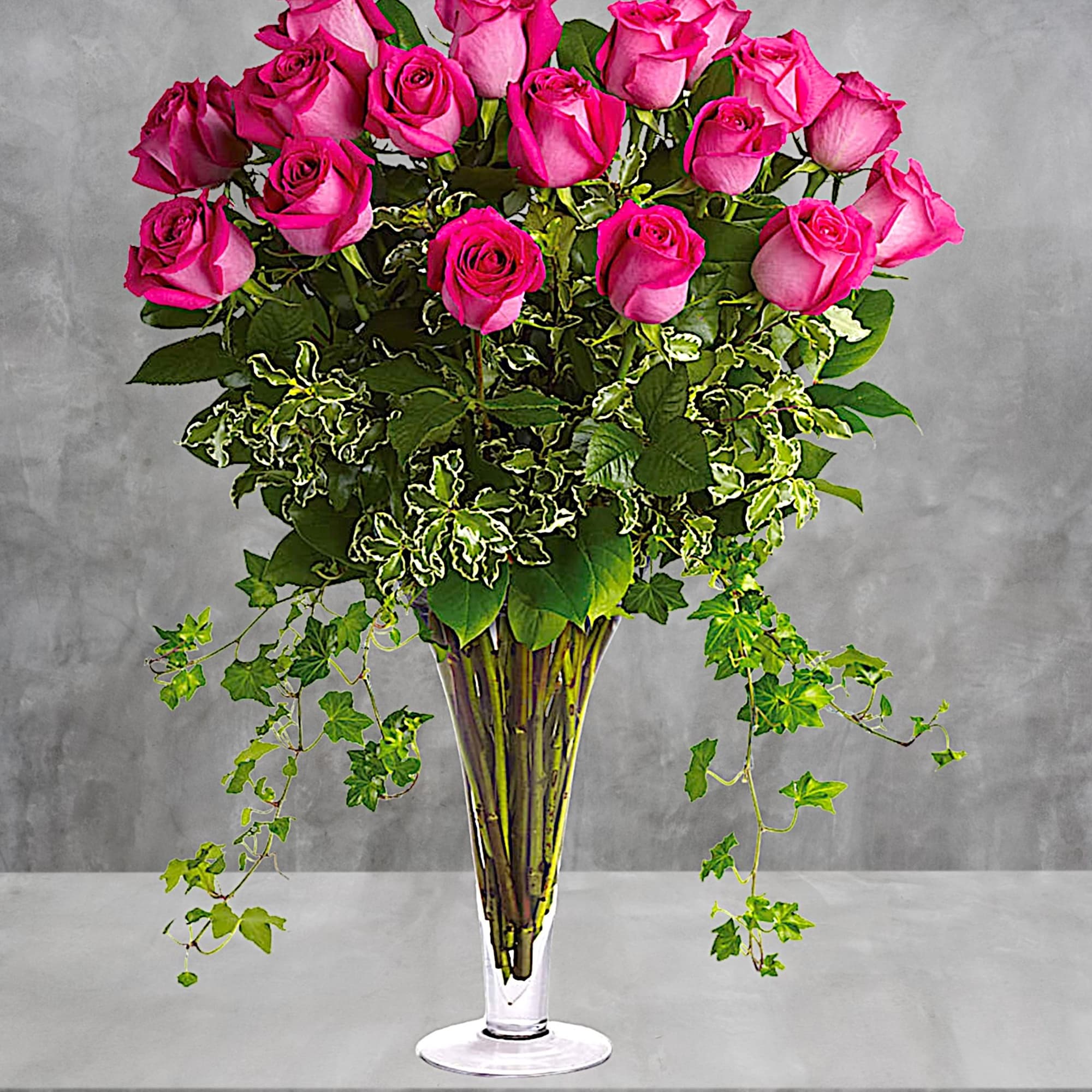 Tall bouquet of pink roses in a clear glass vase with trailing ivy