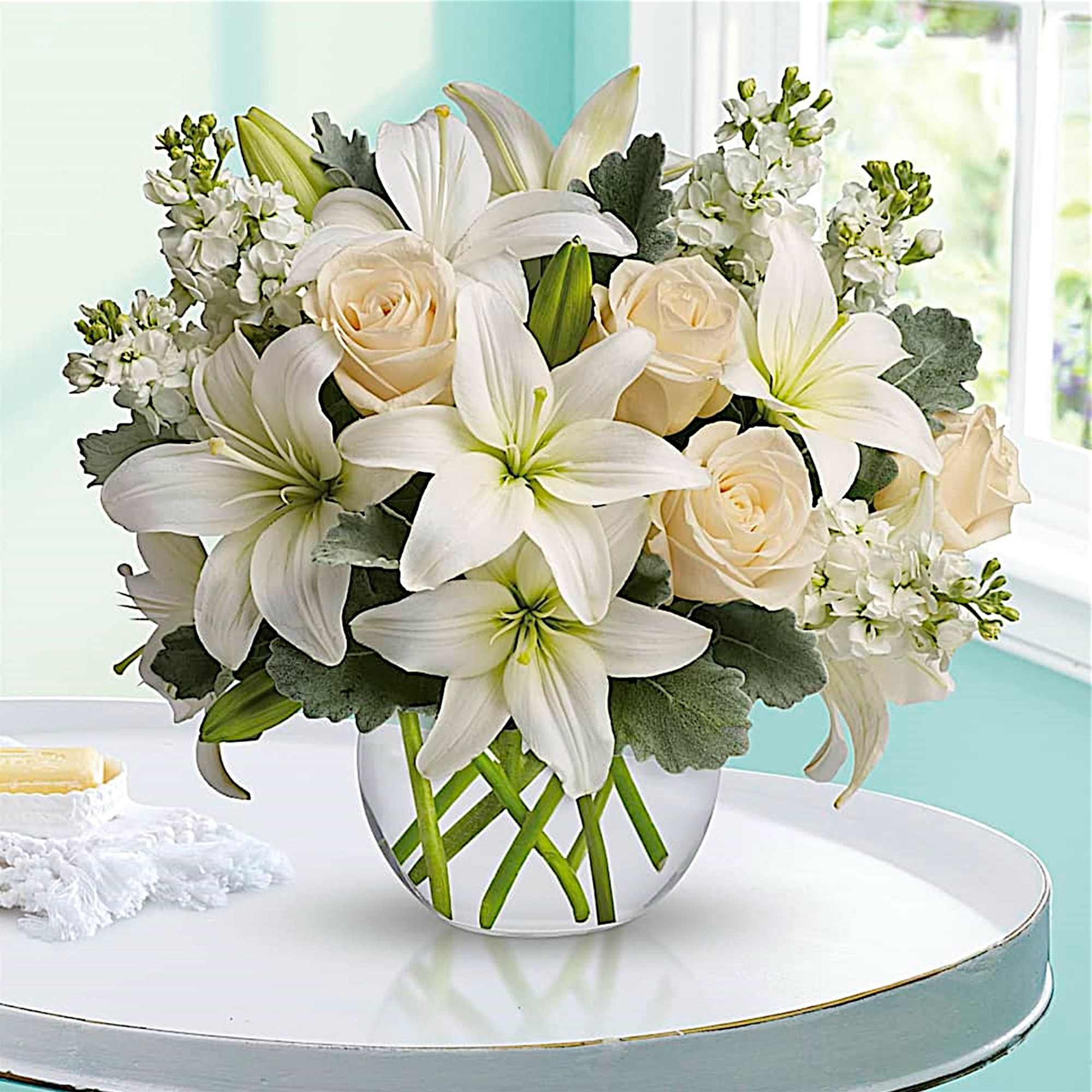White lilies and cream roses arranged in a clear glass vase