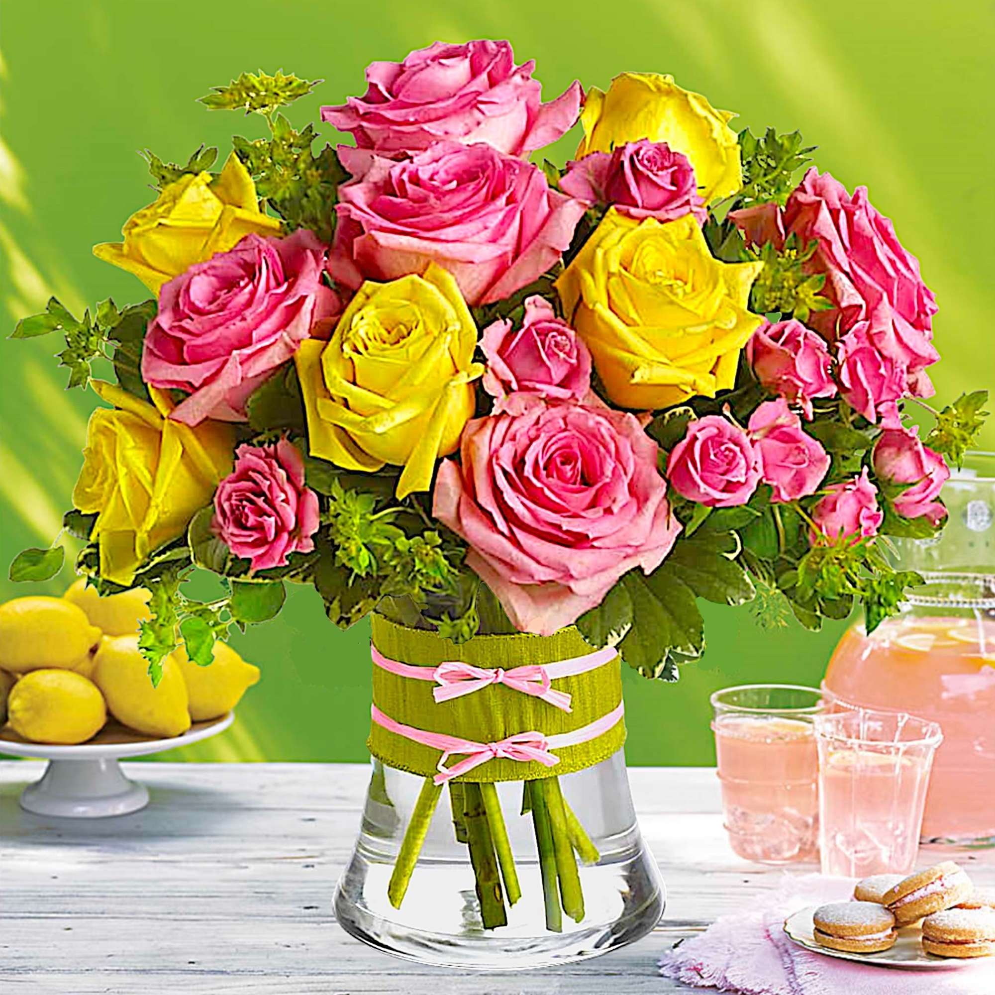 Pink and yellow roses arranged in a glass vase with ribbon