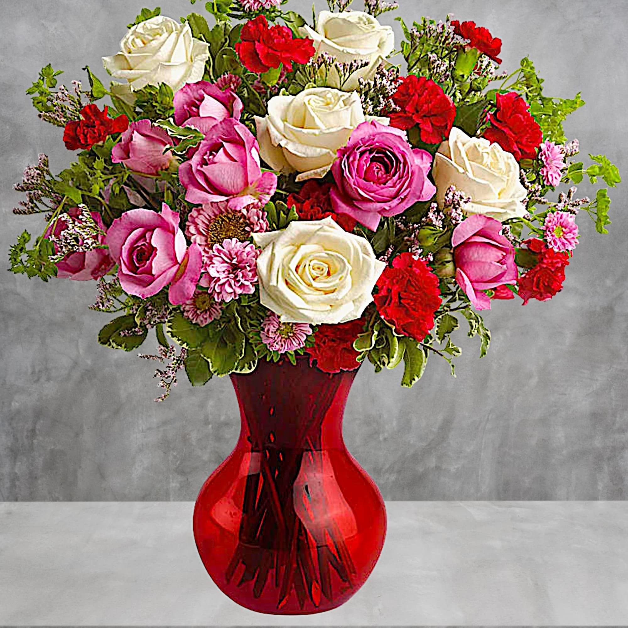 Bouquet of pink and white roses with red carnations in a red glass vase