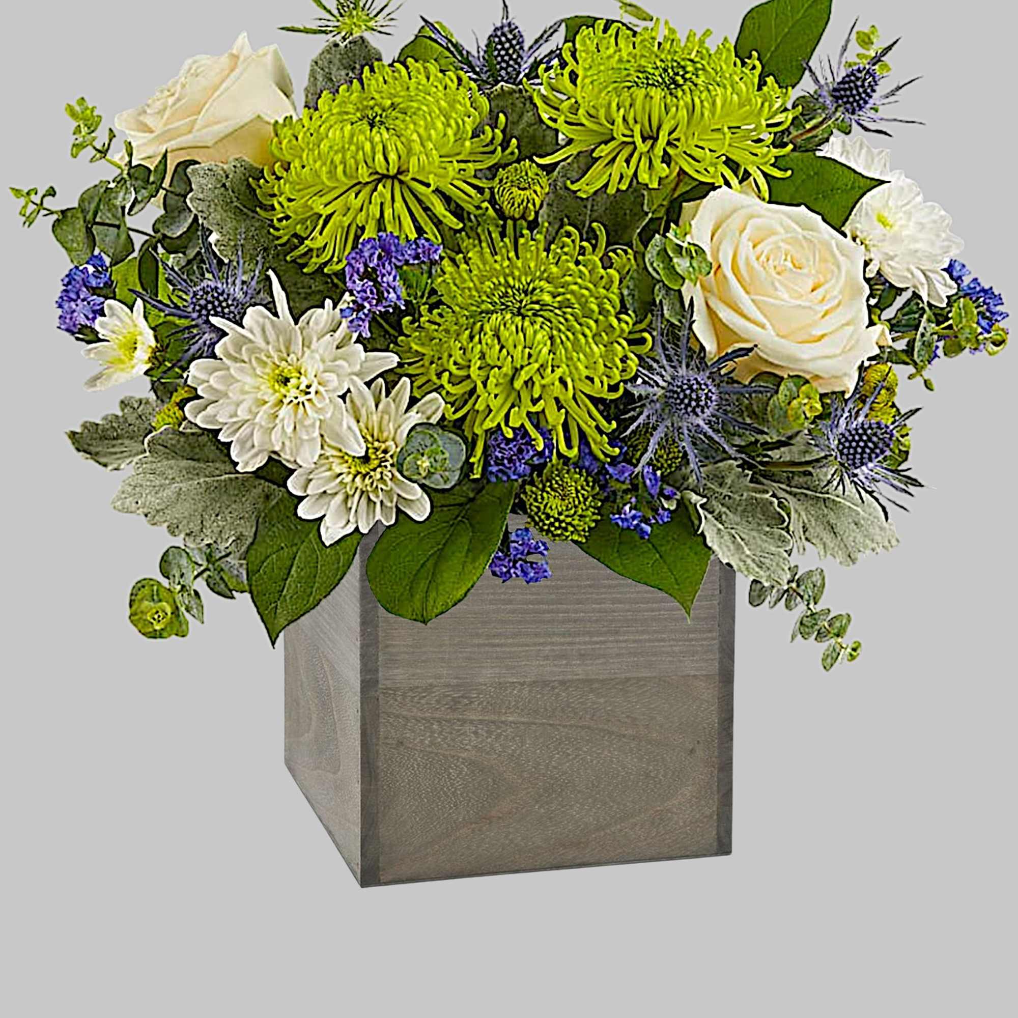 Arrangement of white roses, green chrysanthemums, and blue thistles in a wooden cube vase