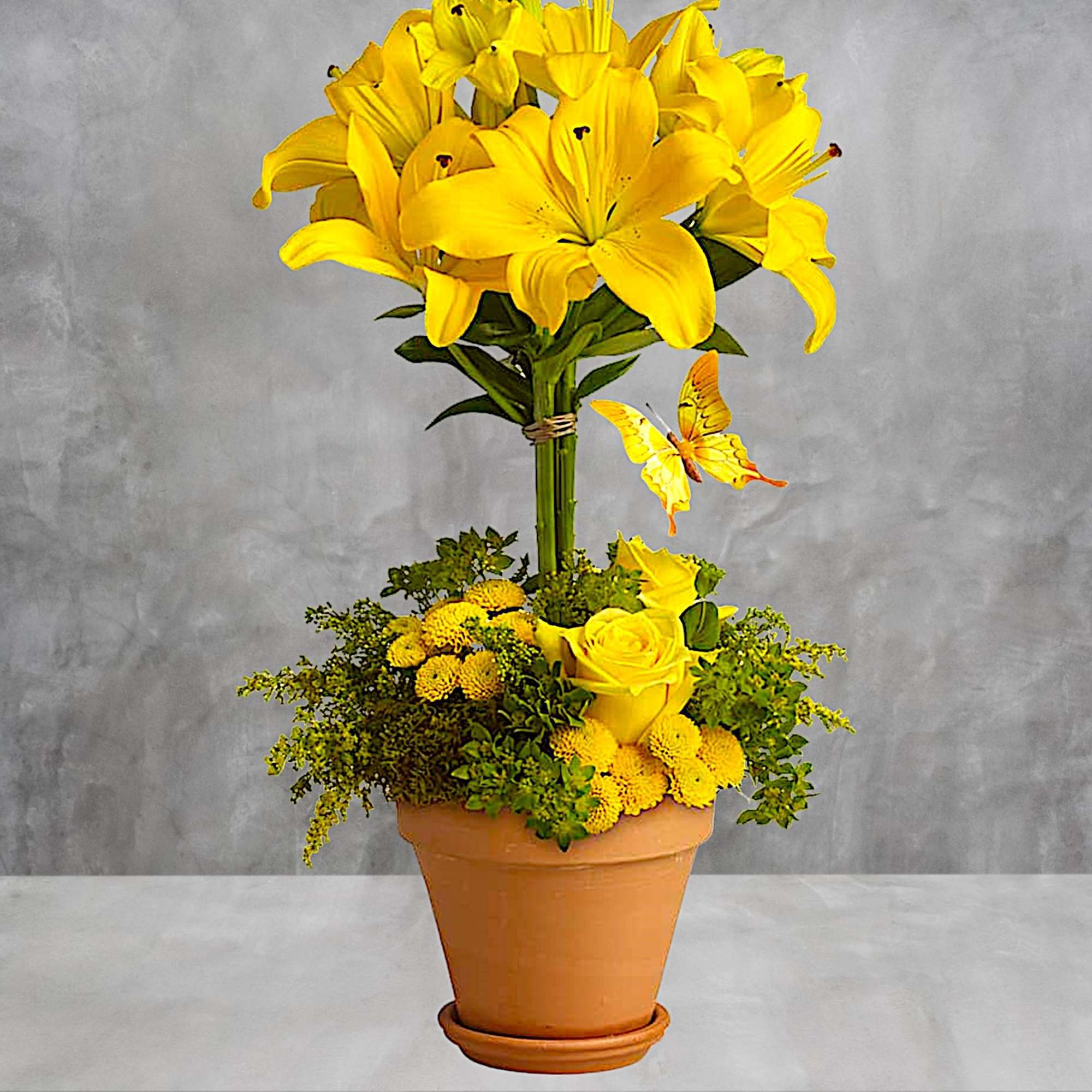 Yellow lilies and roses in a terracotta pot with a butterfly decoration