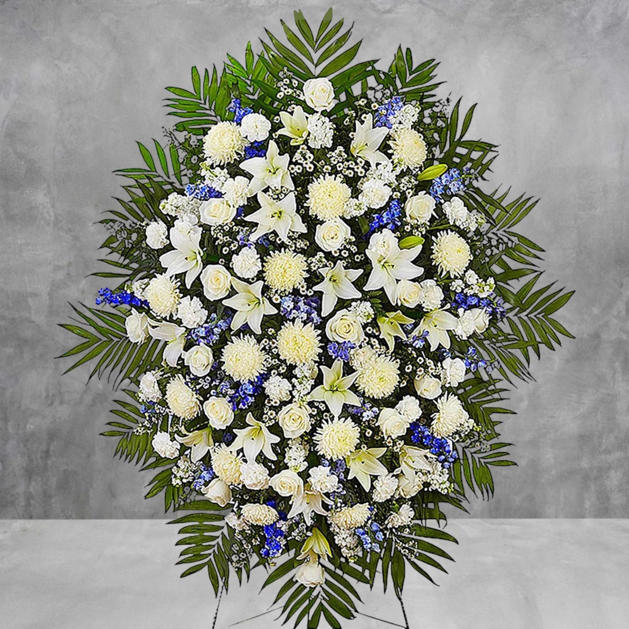 Standing funeral spray of white lilies, roses, and blue accents