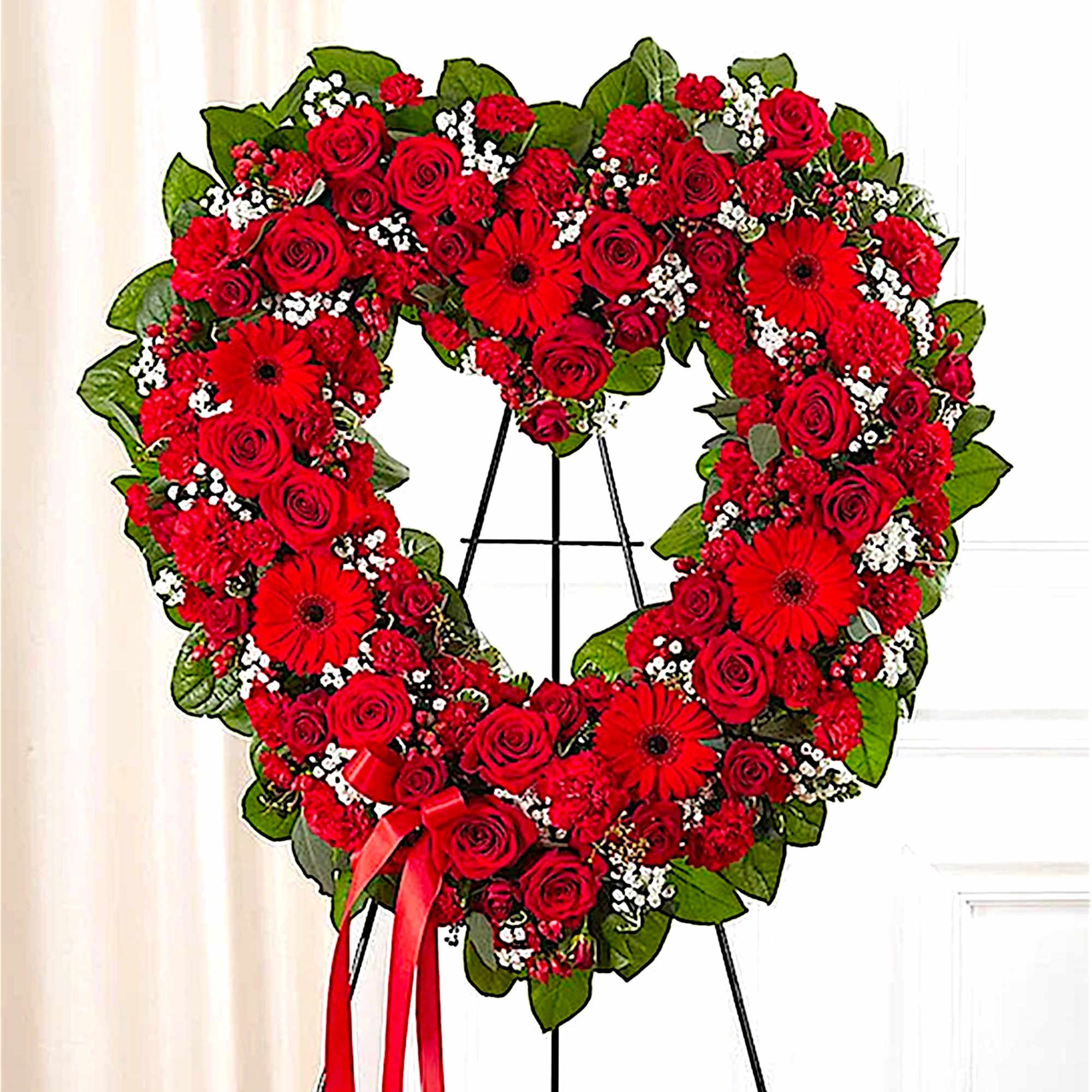 Heart-shaped red floral wreath on a black stand with a ribbon