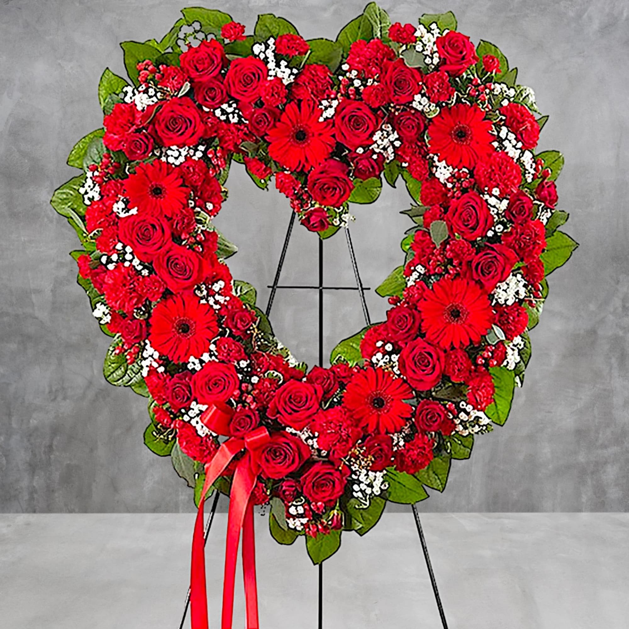 Heart-shaped wreath of red roses and gerbera daisies on a stand