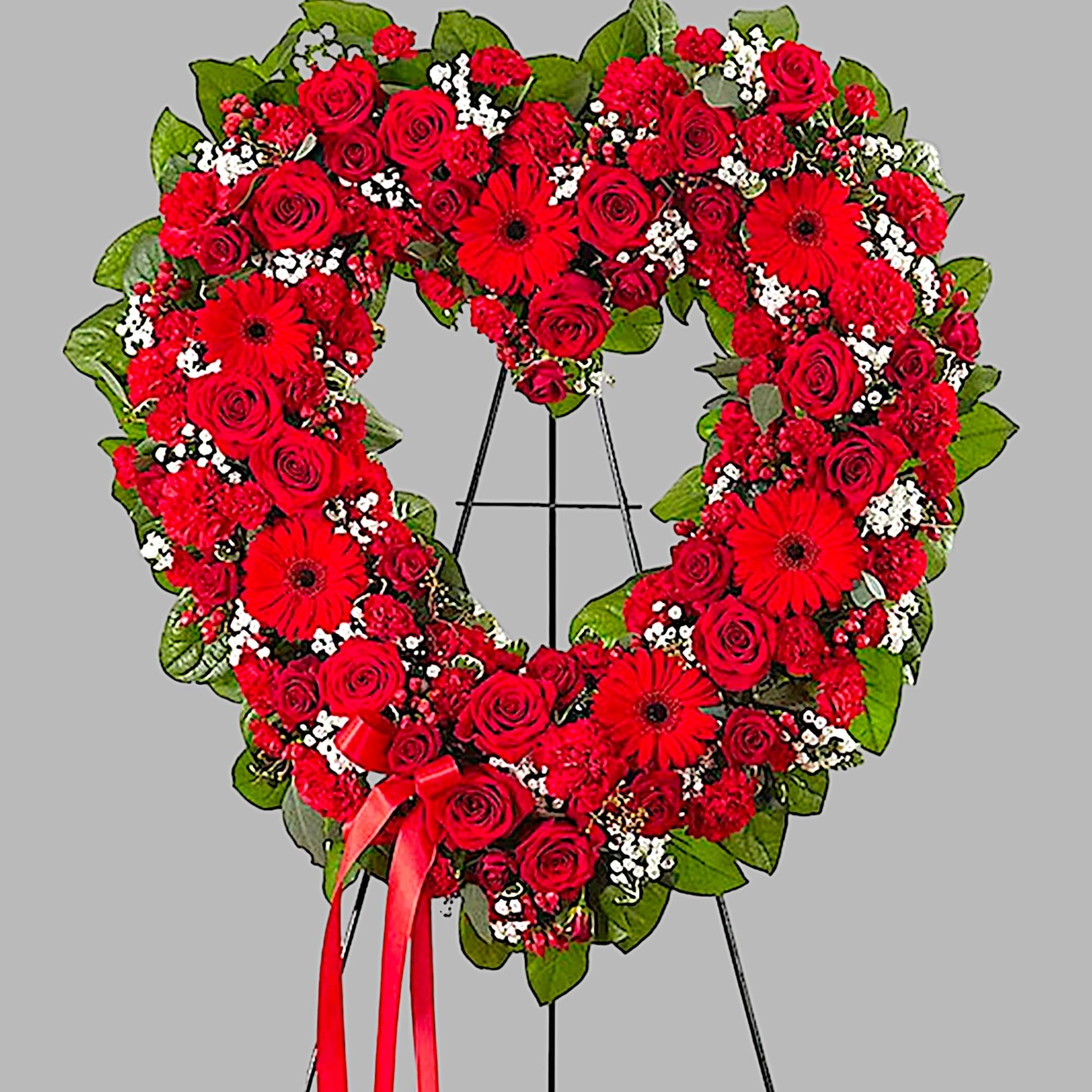 Heart-shaped red rose wreath on a stand with a ribbon bow