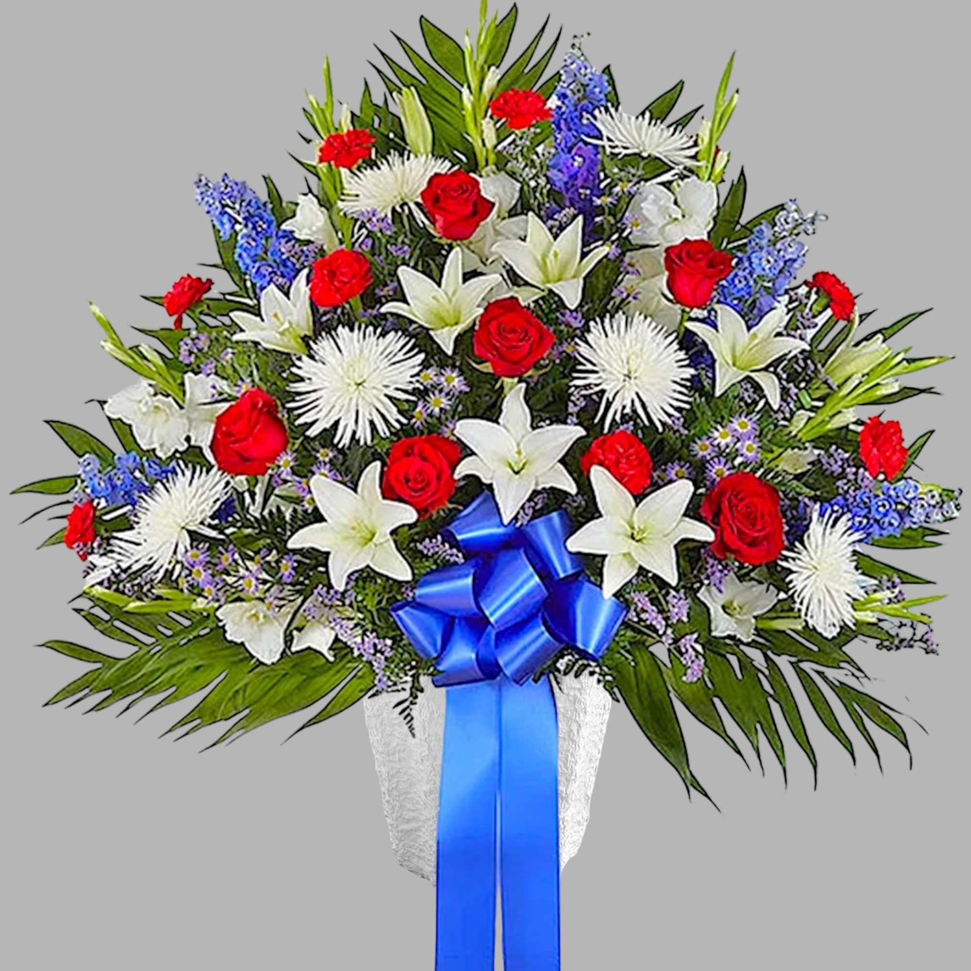 Standing floral spray with red roses, white lilies, and blue accents on a white easel