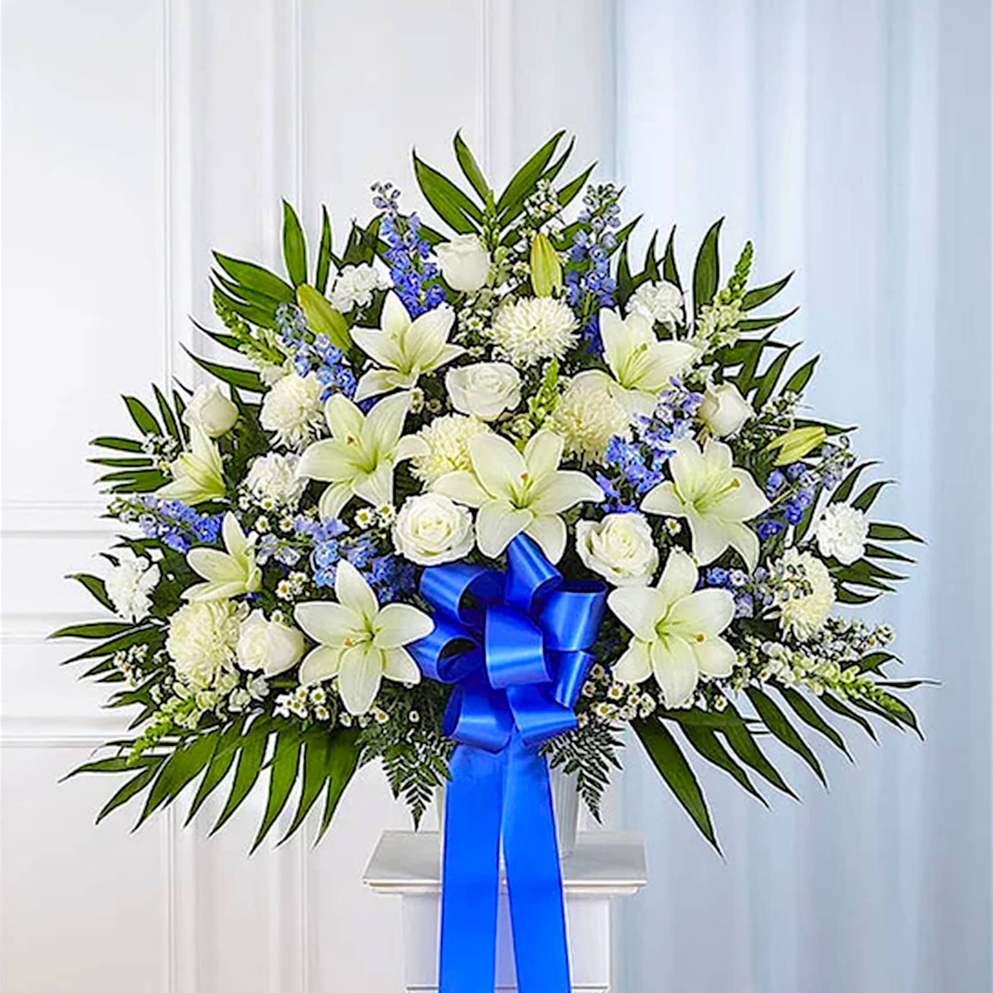 White lily and rose arrangement with blue ribbon in a vase