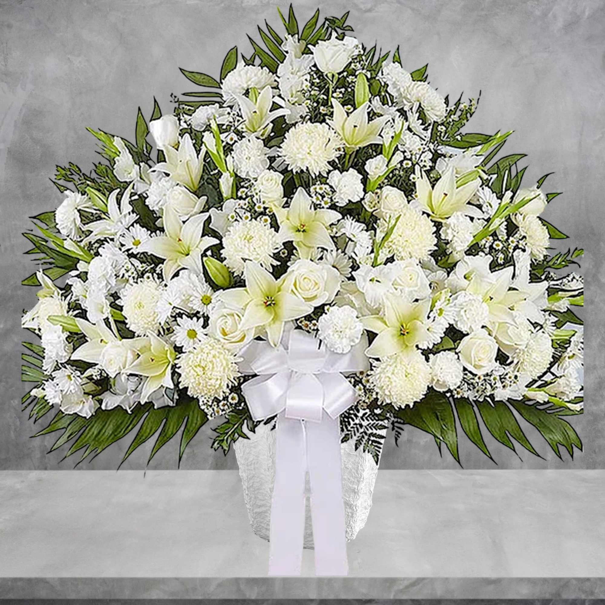 White floral spray with lilies, roses, and chrysanthemums in a vase with a ribbon
