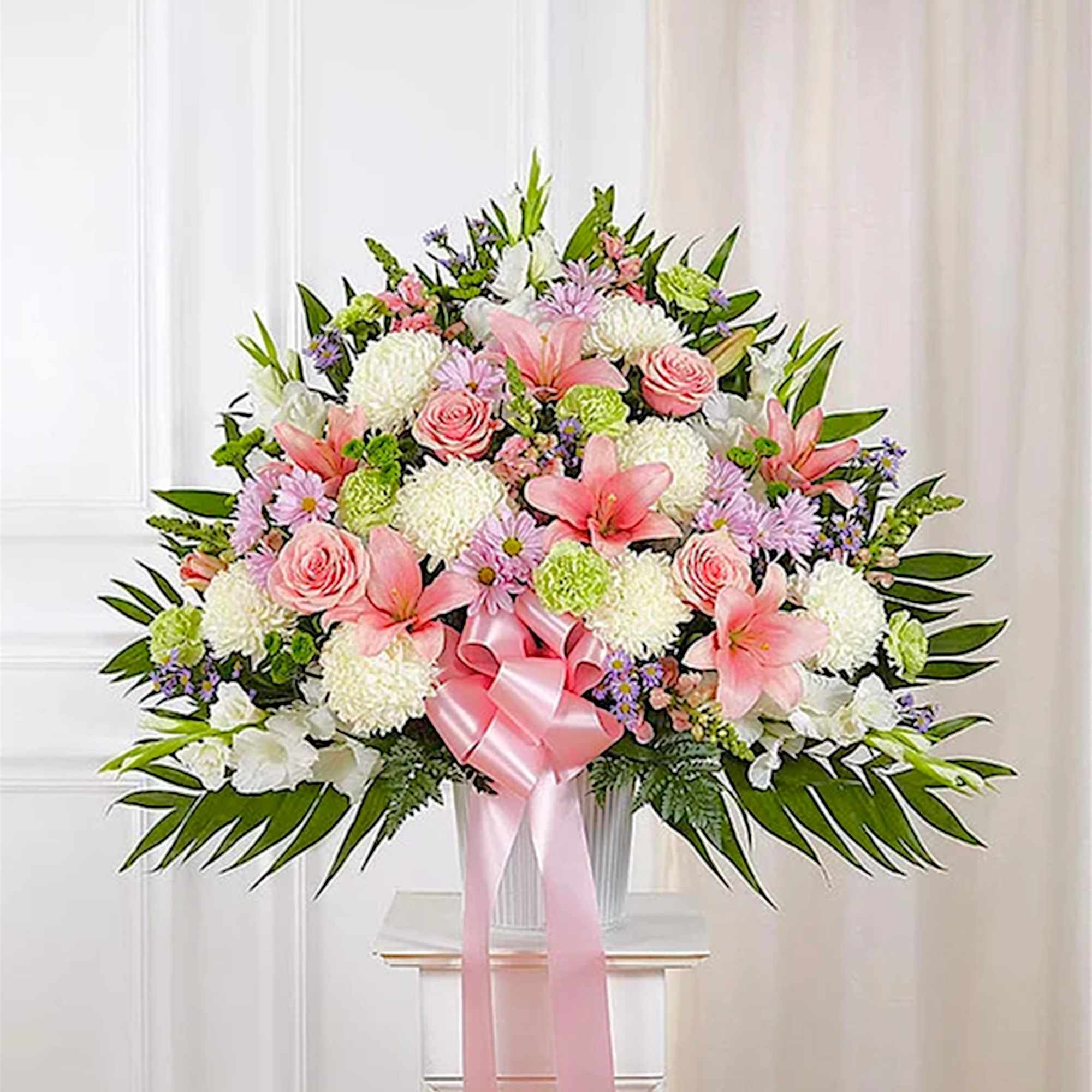 Large pink and white floral arrangement with a pink ribbon in a white vase