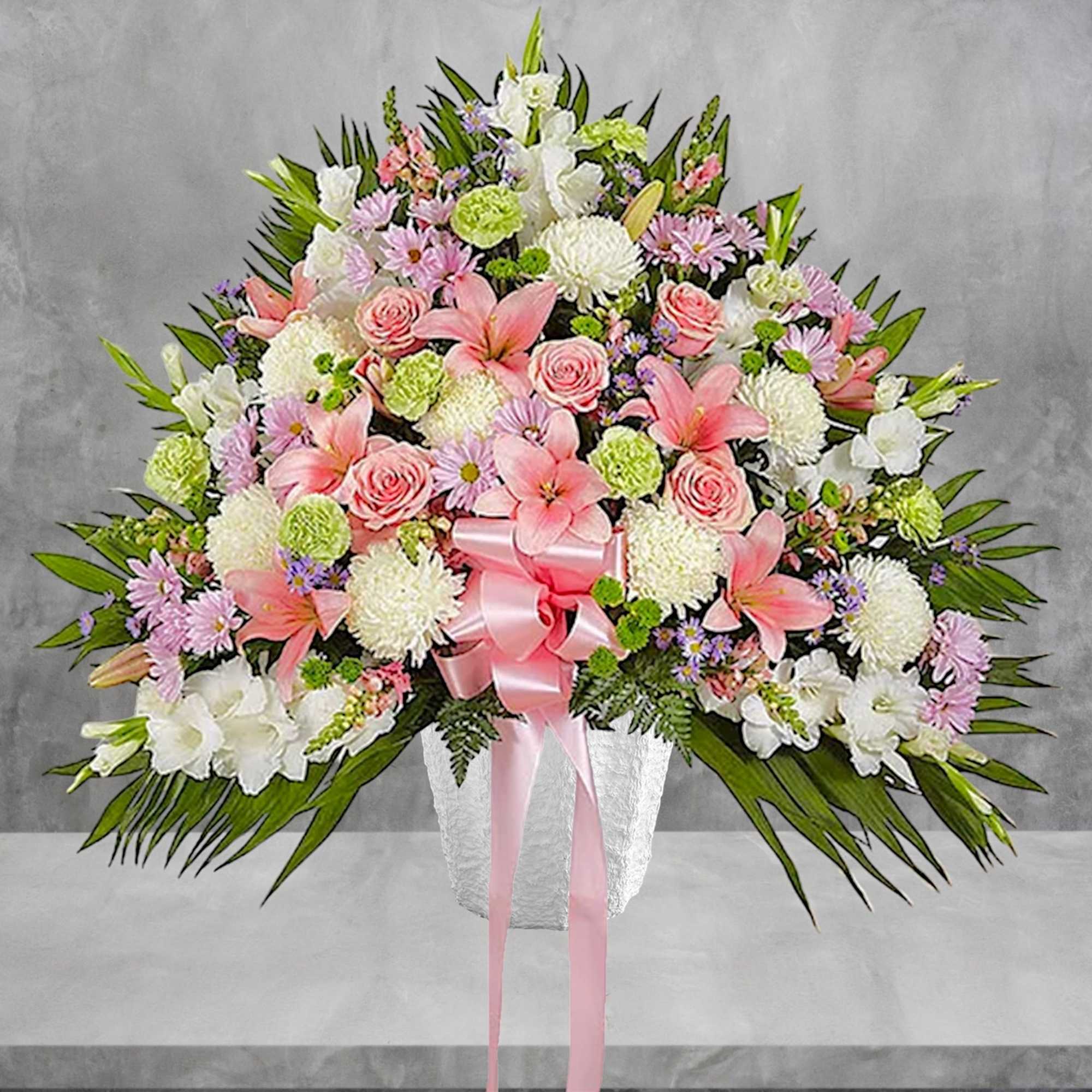 Large mixed floral arrangement in a white vase with a pink ribbon
