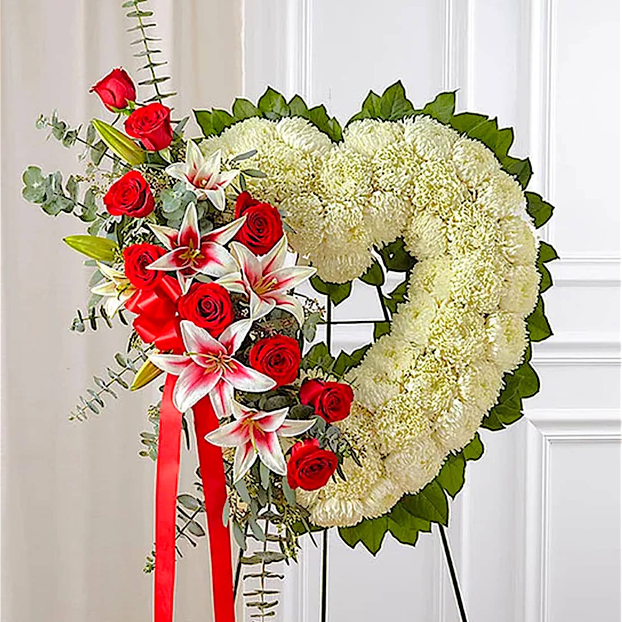 Heart-shaped floral wreath with red roses and white lilies on an easel