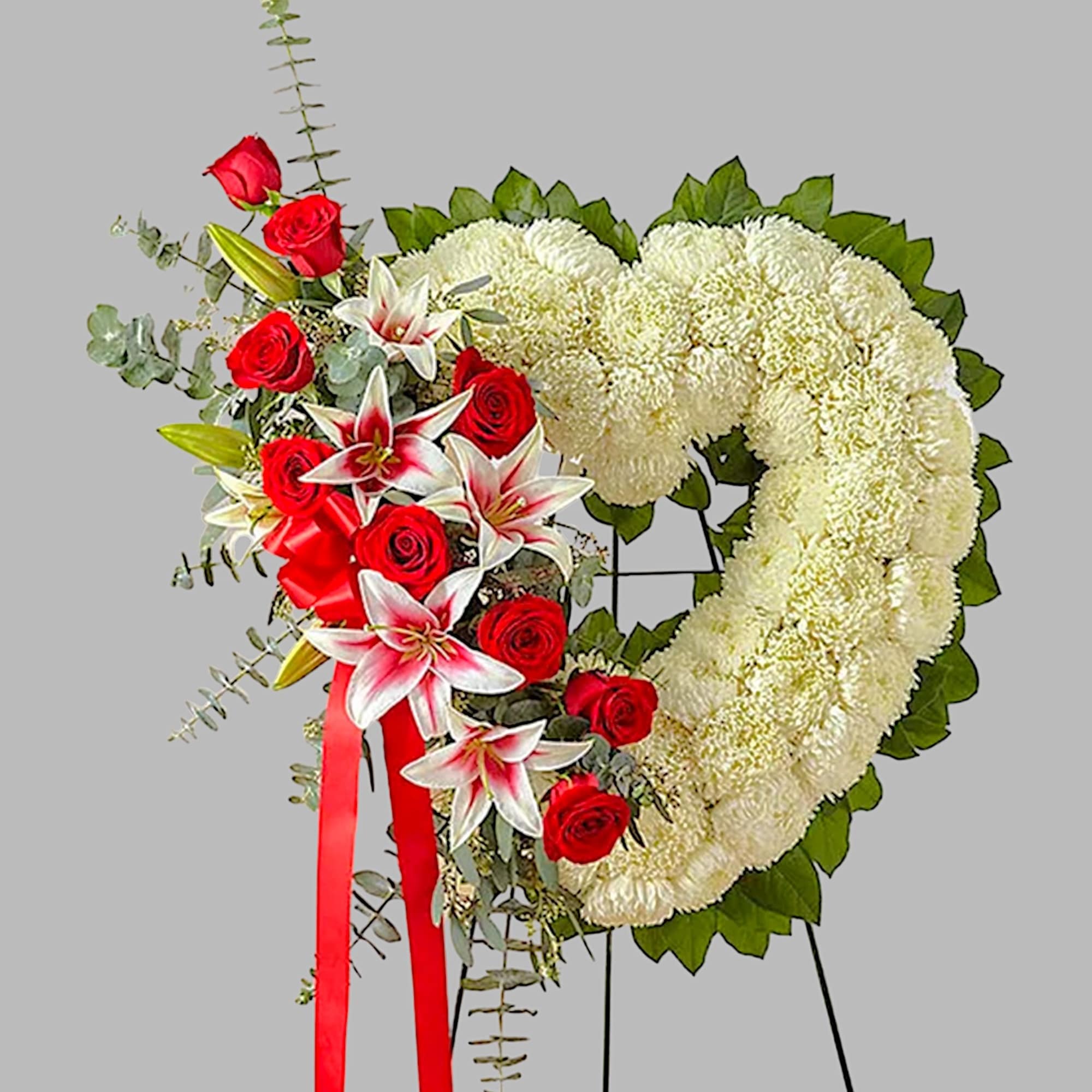 Heart-shaped floral wreath with red roses and white lilies on a stand
