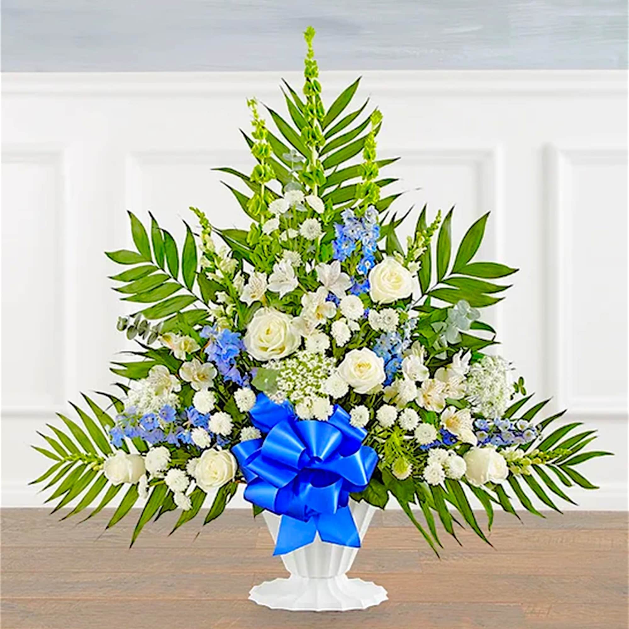 White floral standing arrangement with blue ribbon in a pedestal vase