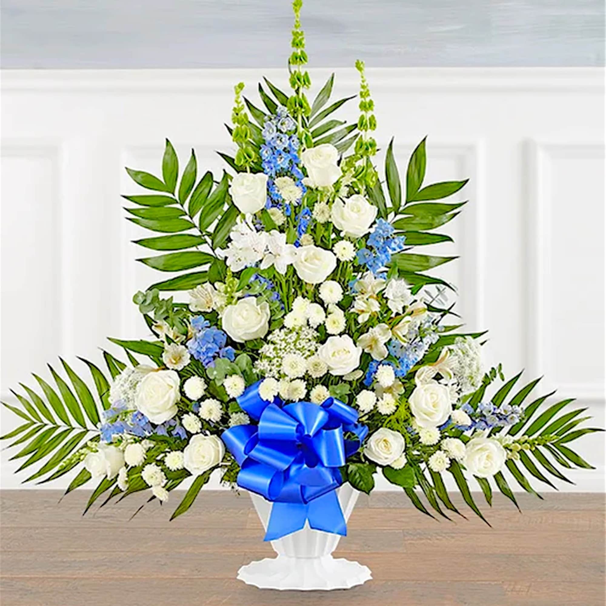 White floral standing spray with blue ribbon in a pedestal vase