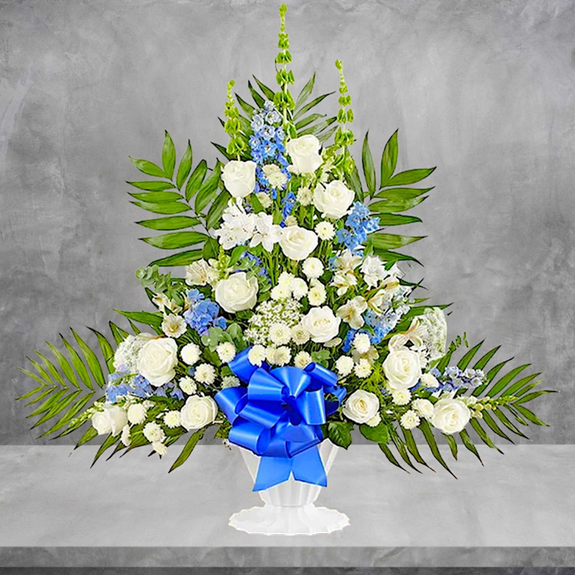 Tall white and blue floral arrangement in a white pedestal vase with a blue bow