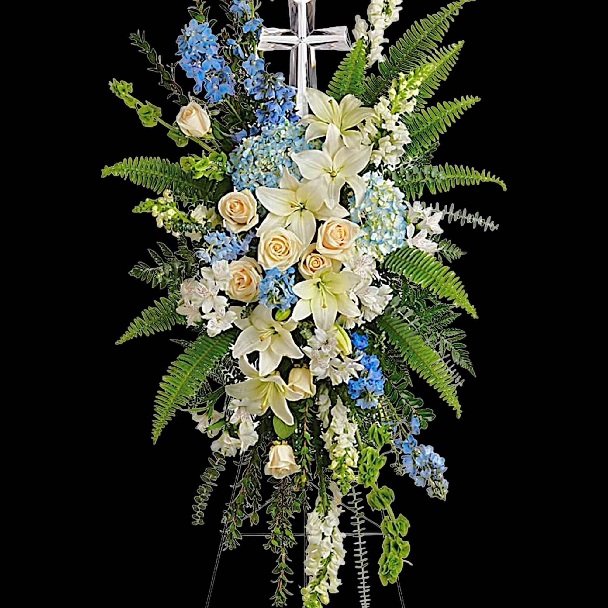 Tall floral standing spray with white lilies, blue flowers, and a cross