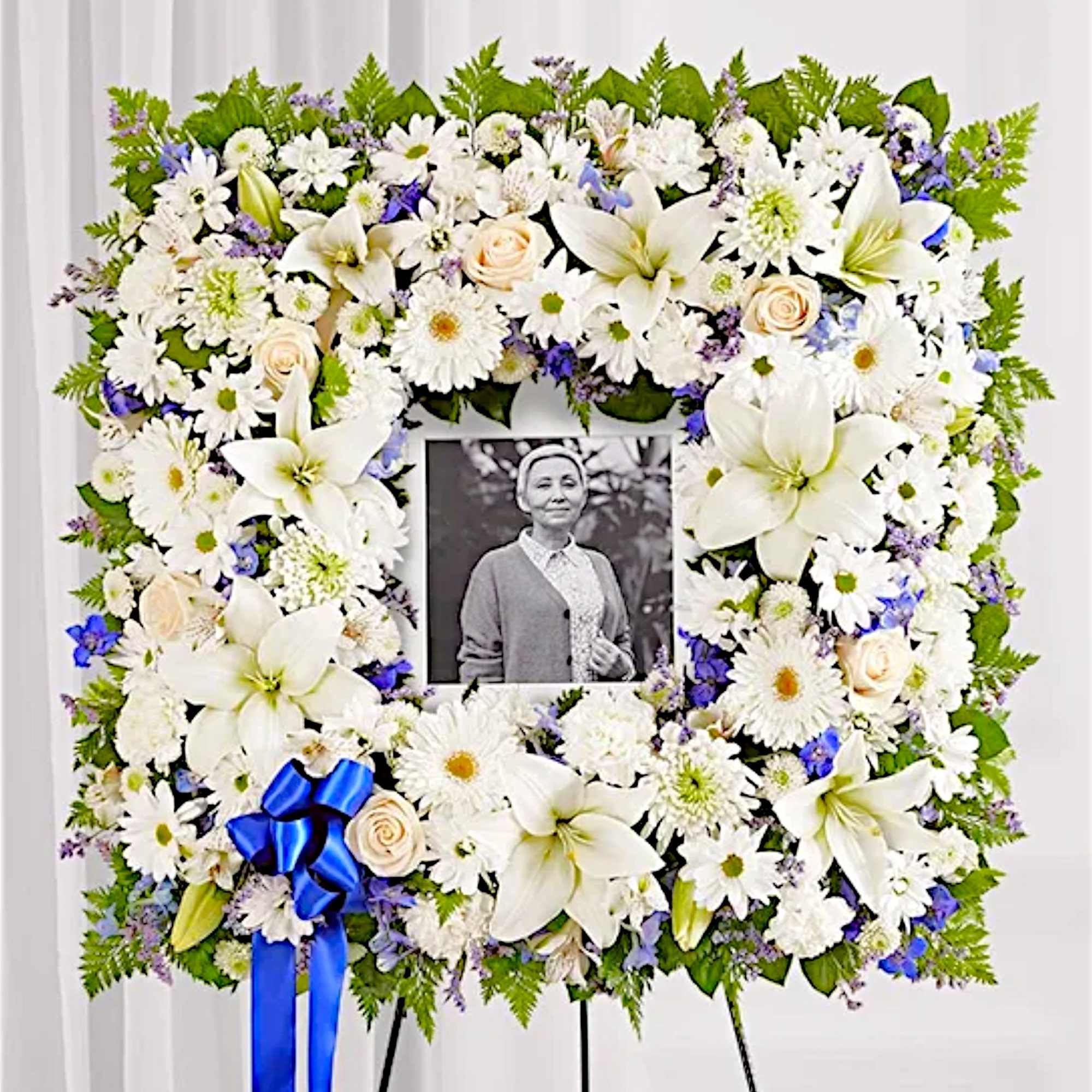 White floral funeral wreath with a photo in the center and a blue ribbon