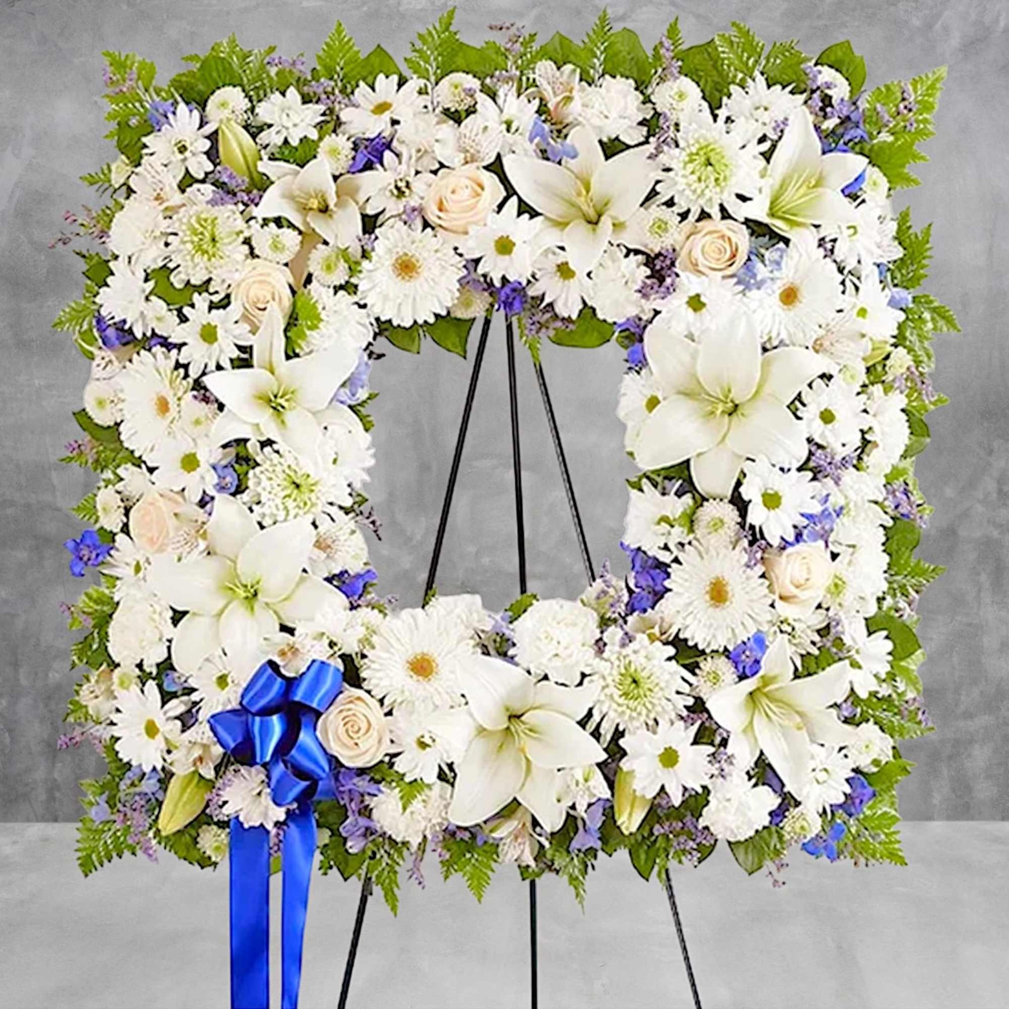 White floral wreath on a black easel with a blue ribbon