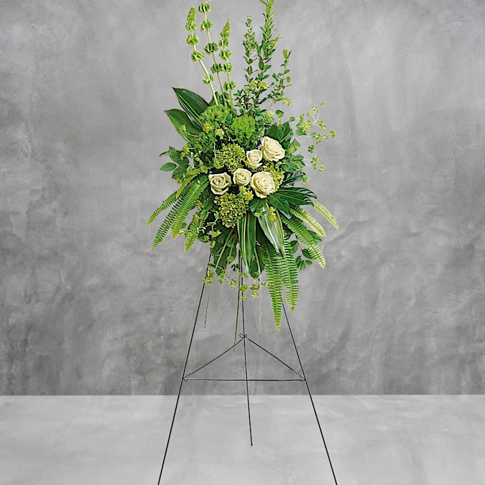 Tall floral spray with white roses and green foliage on a stand