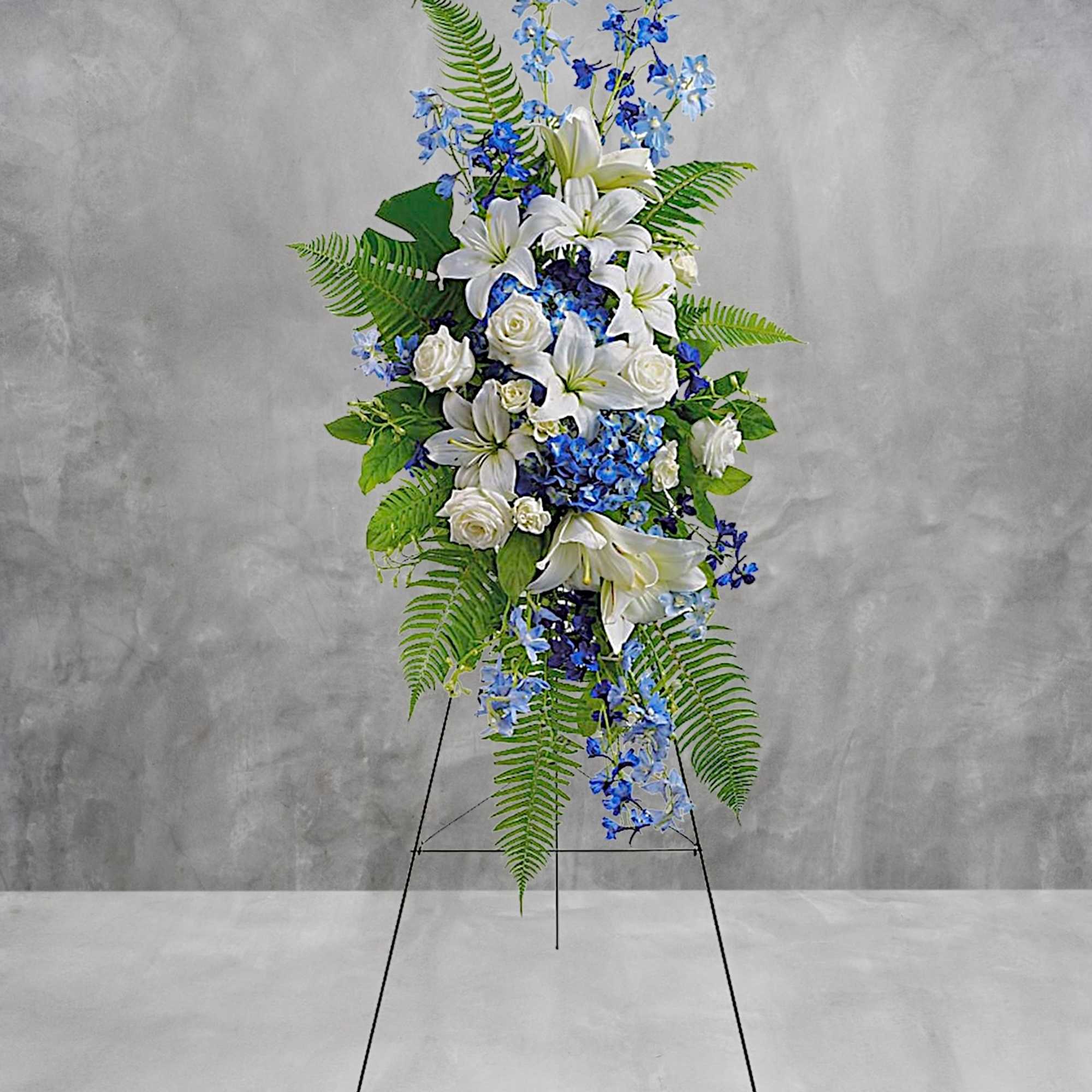 Tall standing floral spray with white lilies, roses, and blue flowers