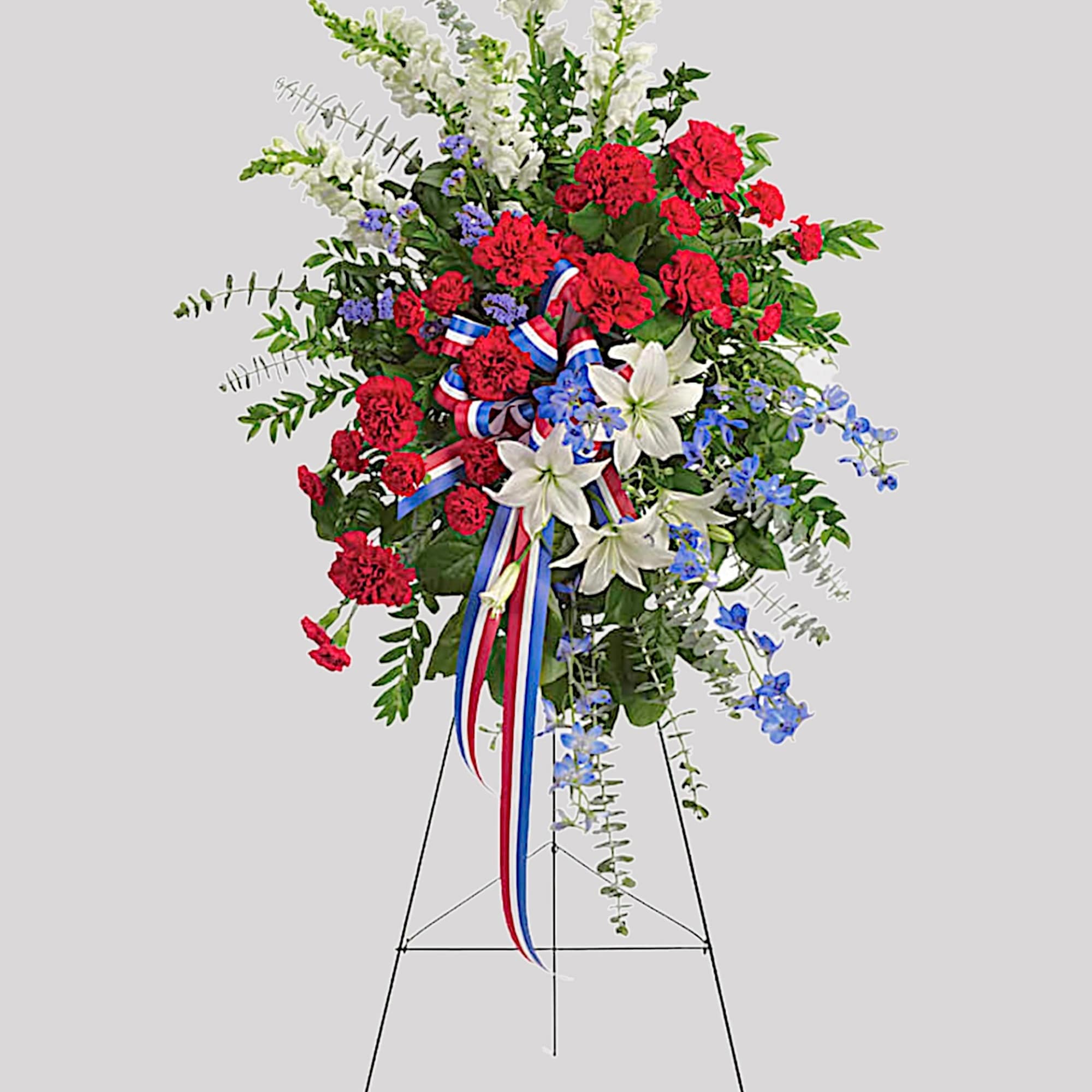 Standing floral spray with red carnations, white lilies, and blue accents on an easel, photo 4 of 4