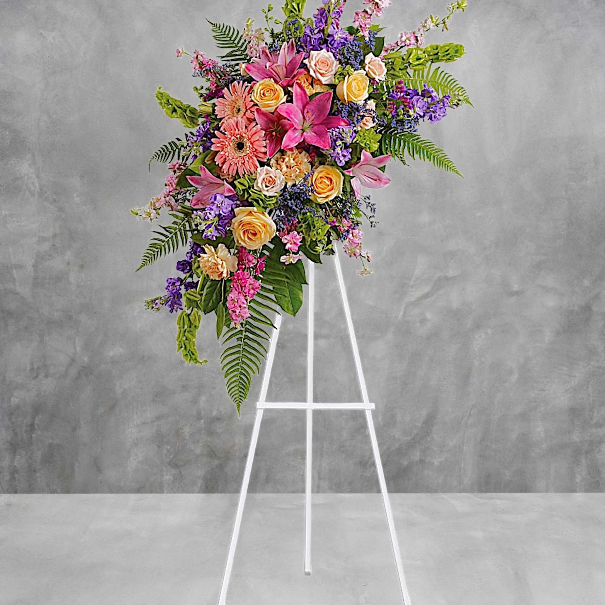 Standing floral spray with pink lilies, roses, and purple blooms on a white easel