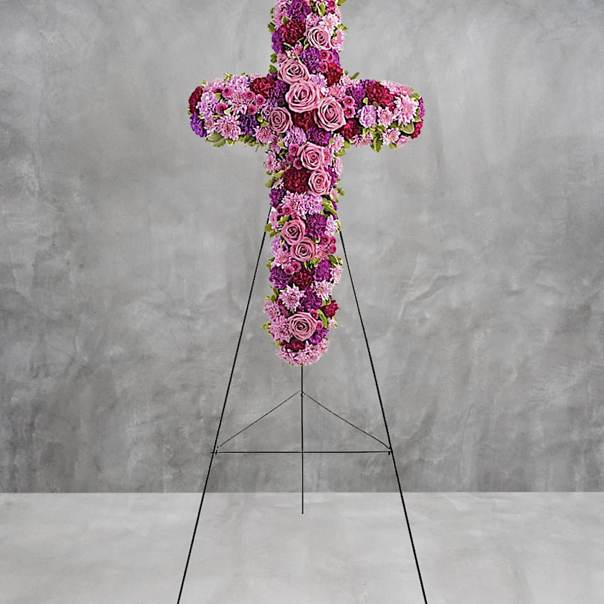 Cross-shaped floral tribute with pink and purple flowers on a stand