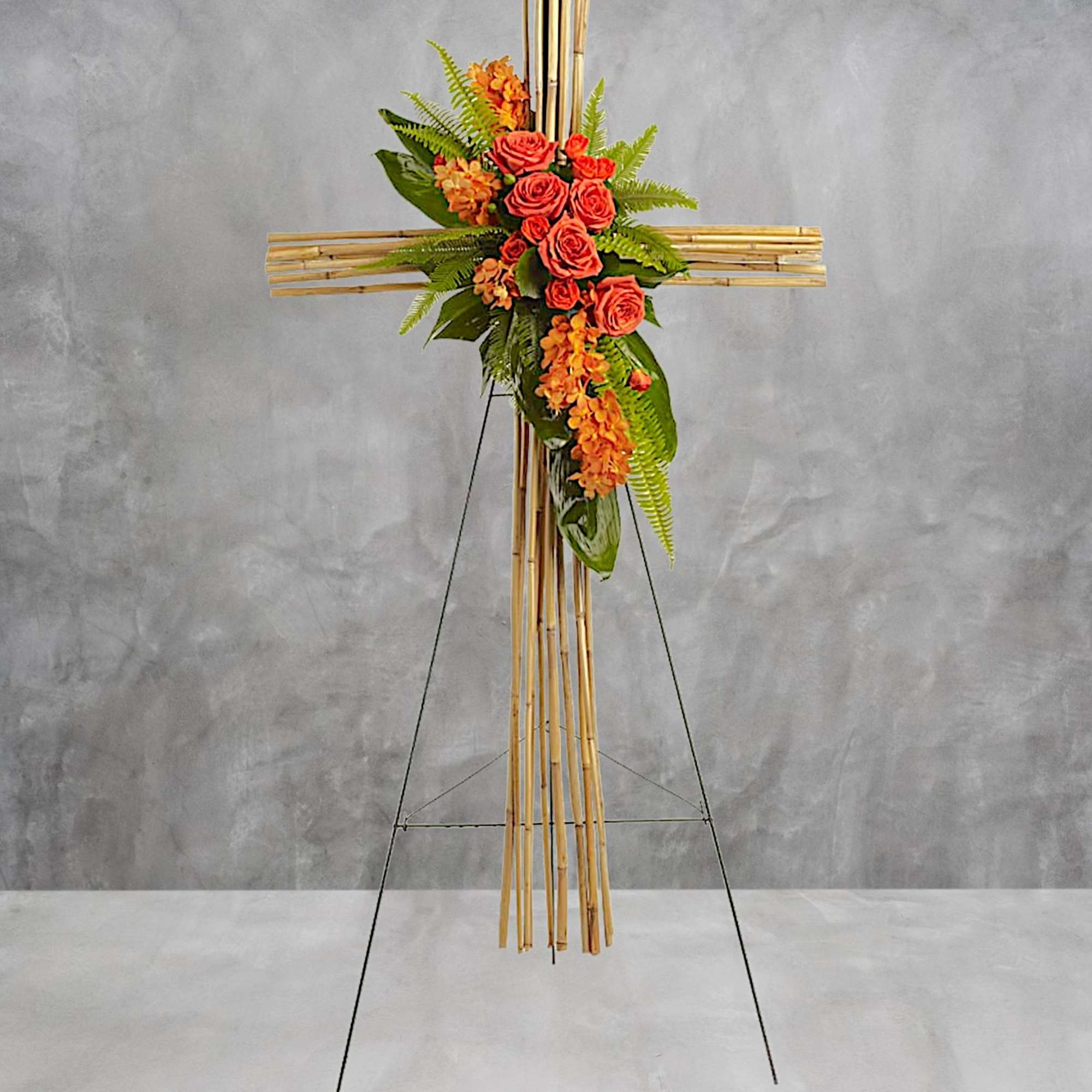 Cross-shaped floral tribute with orange roses and orchids on a bamboo stand