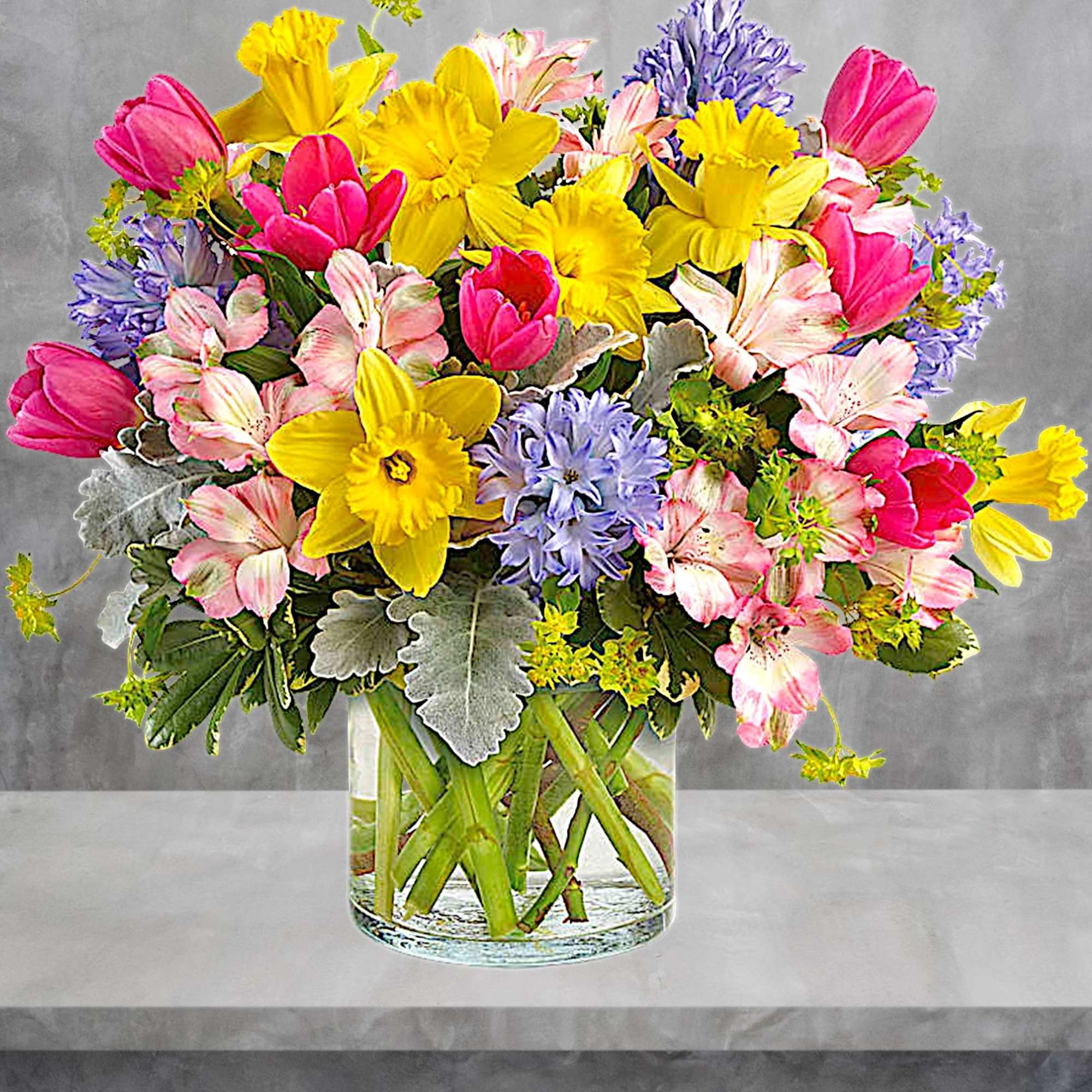 Mixed bouquet of yellow daffodils, pink tulips, and purple flowers in a glass vase