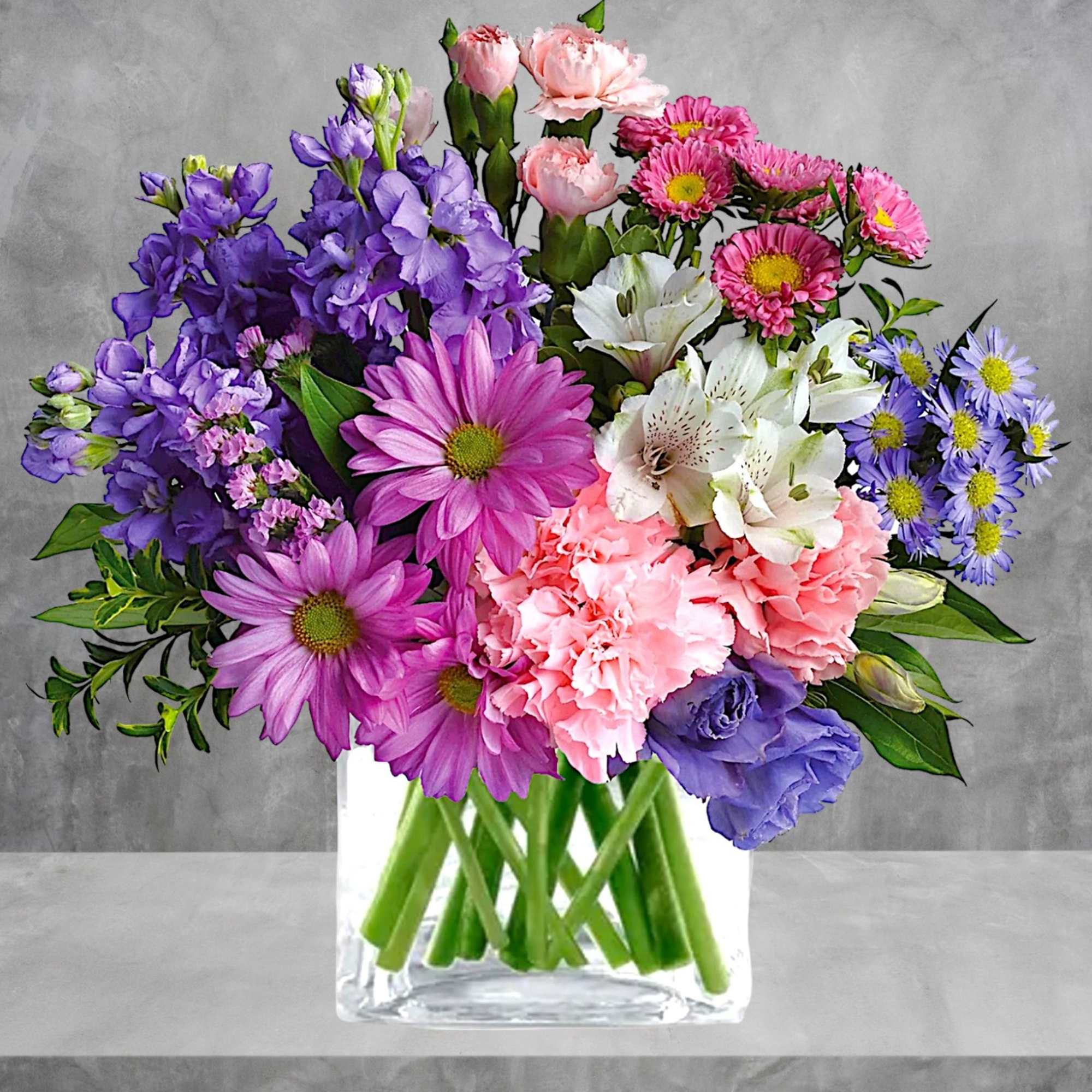 Mixed bouquet of pink, purple, and white flowers in a clear glass vase