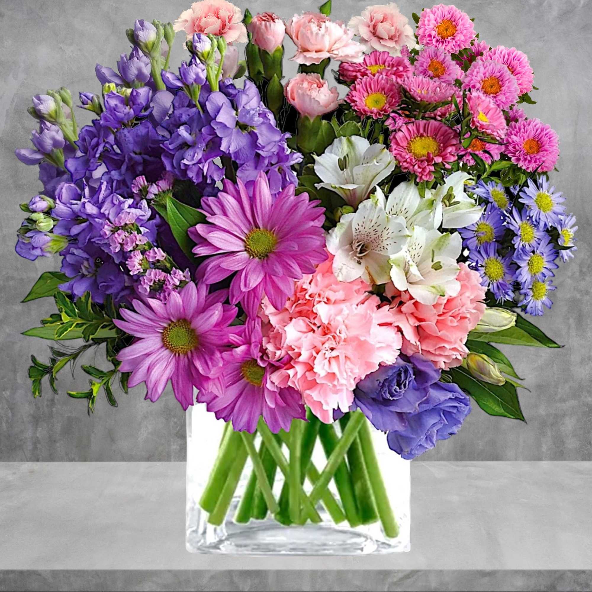 Mixed bouquet of pink, purple, and white flowers in a clear glass vase