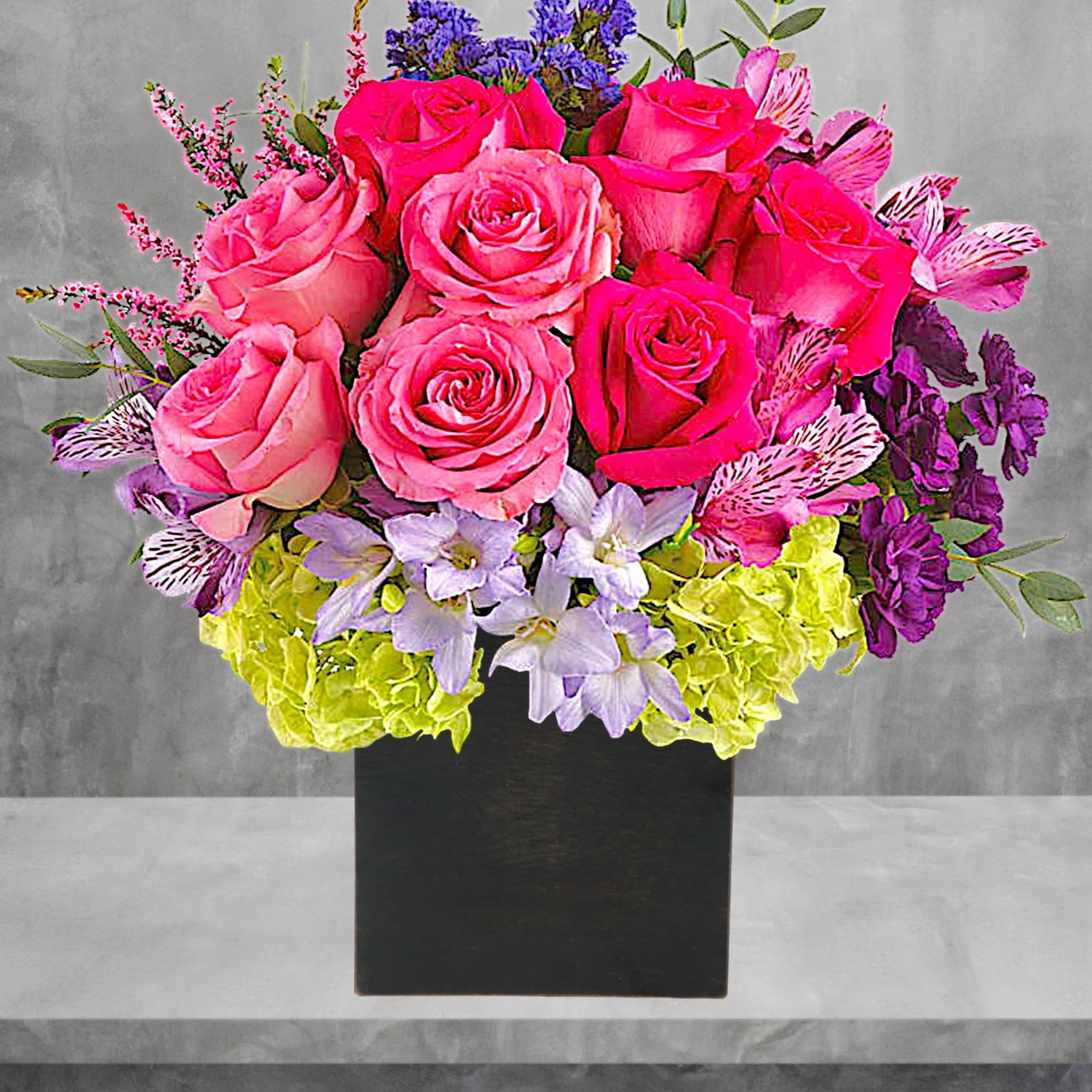 Pink rose bouquet in a black square vase with purple and lime flowers