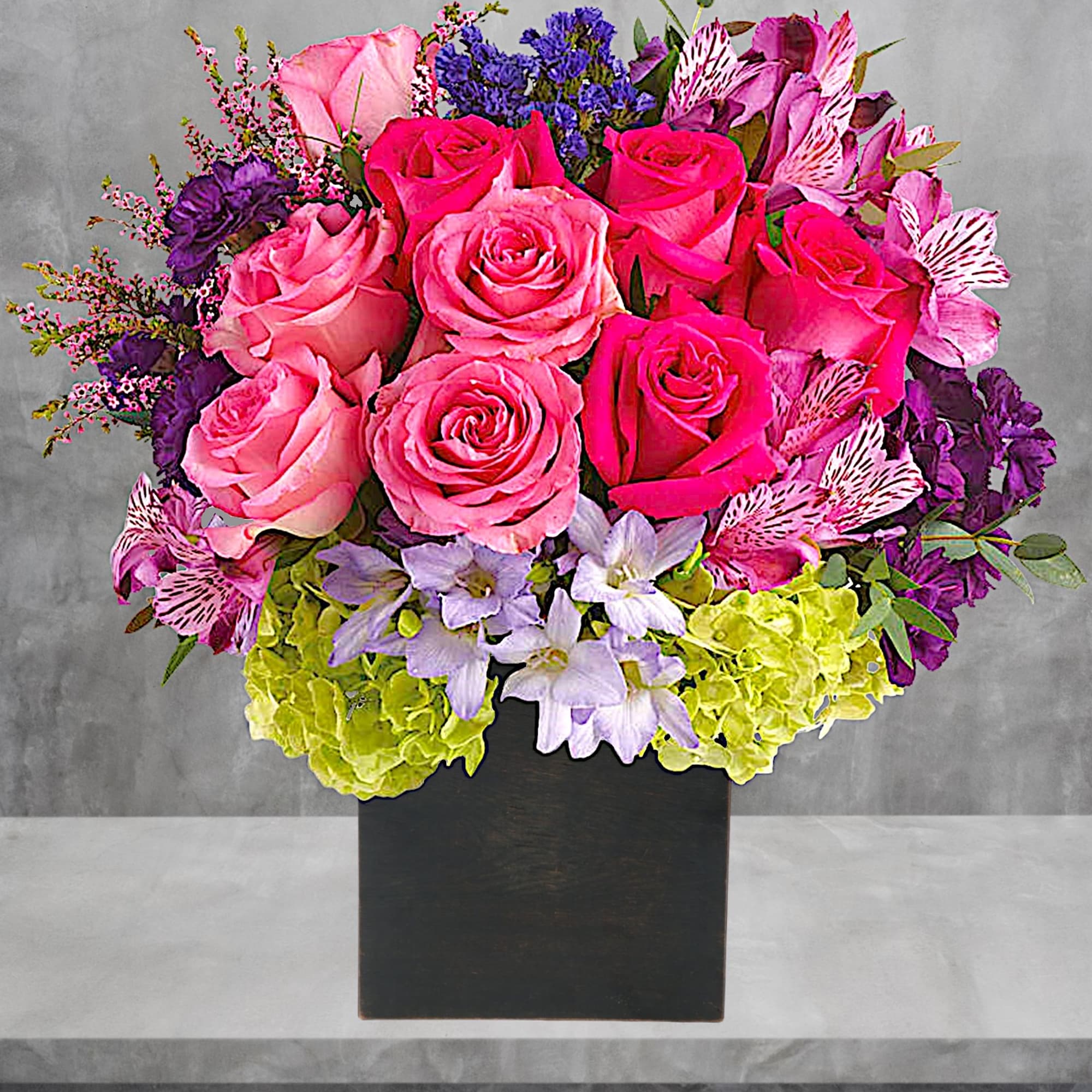 Pink and purple rose arrangement in a black square vase