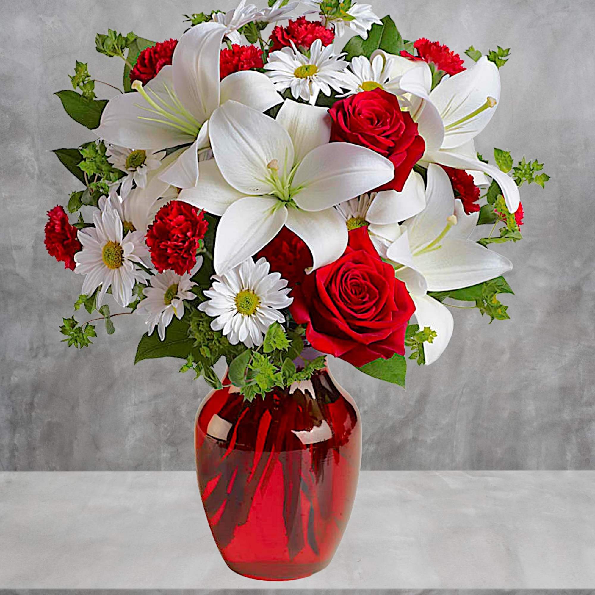 Red roses, white lilies, and daisies arranged in a red glass vase
