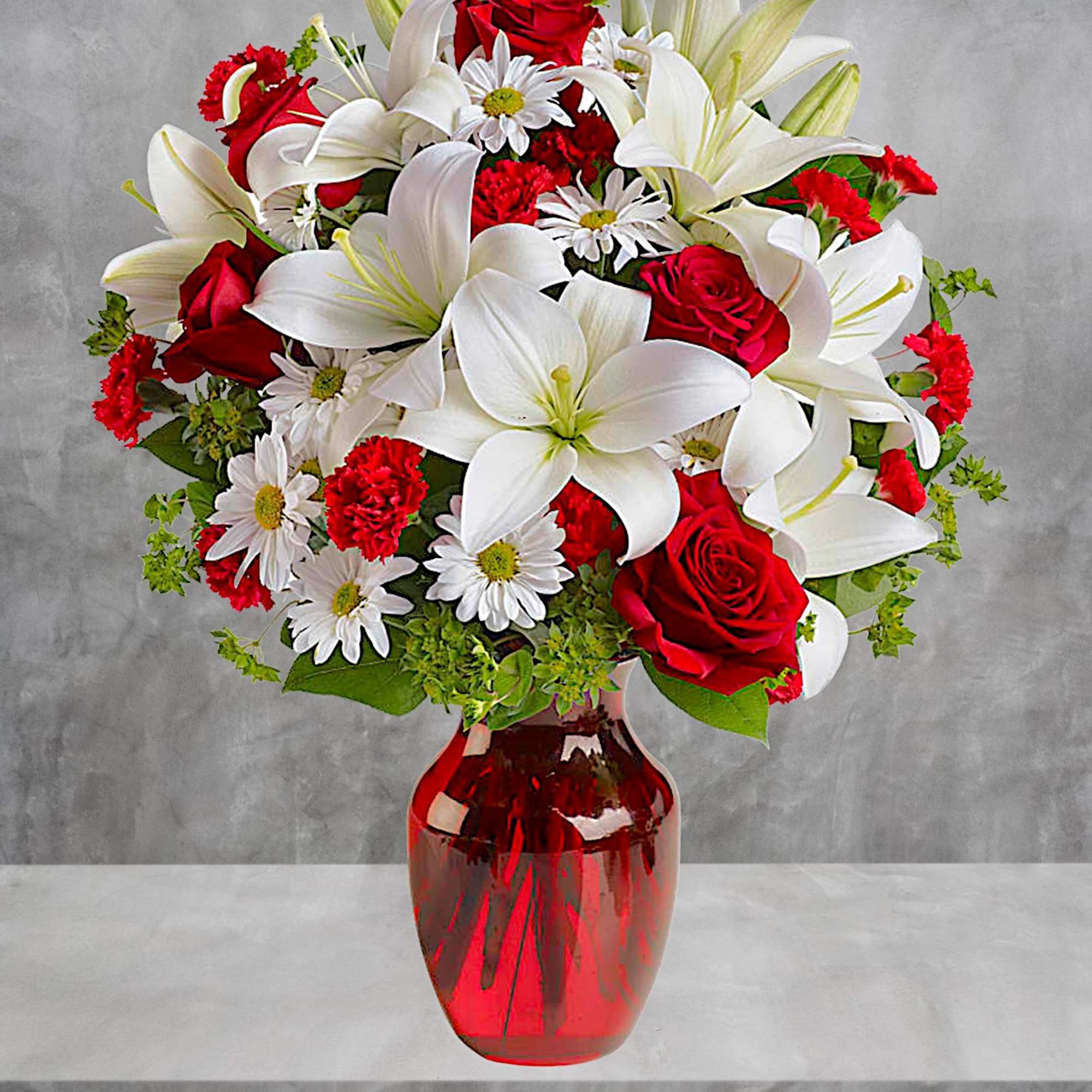 Bouquet of red roses, white lilies, and daisies in a red glass vase