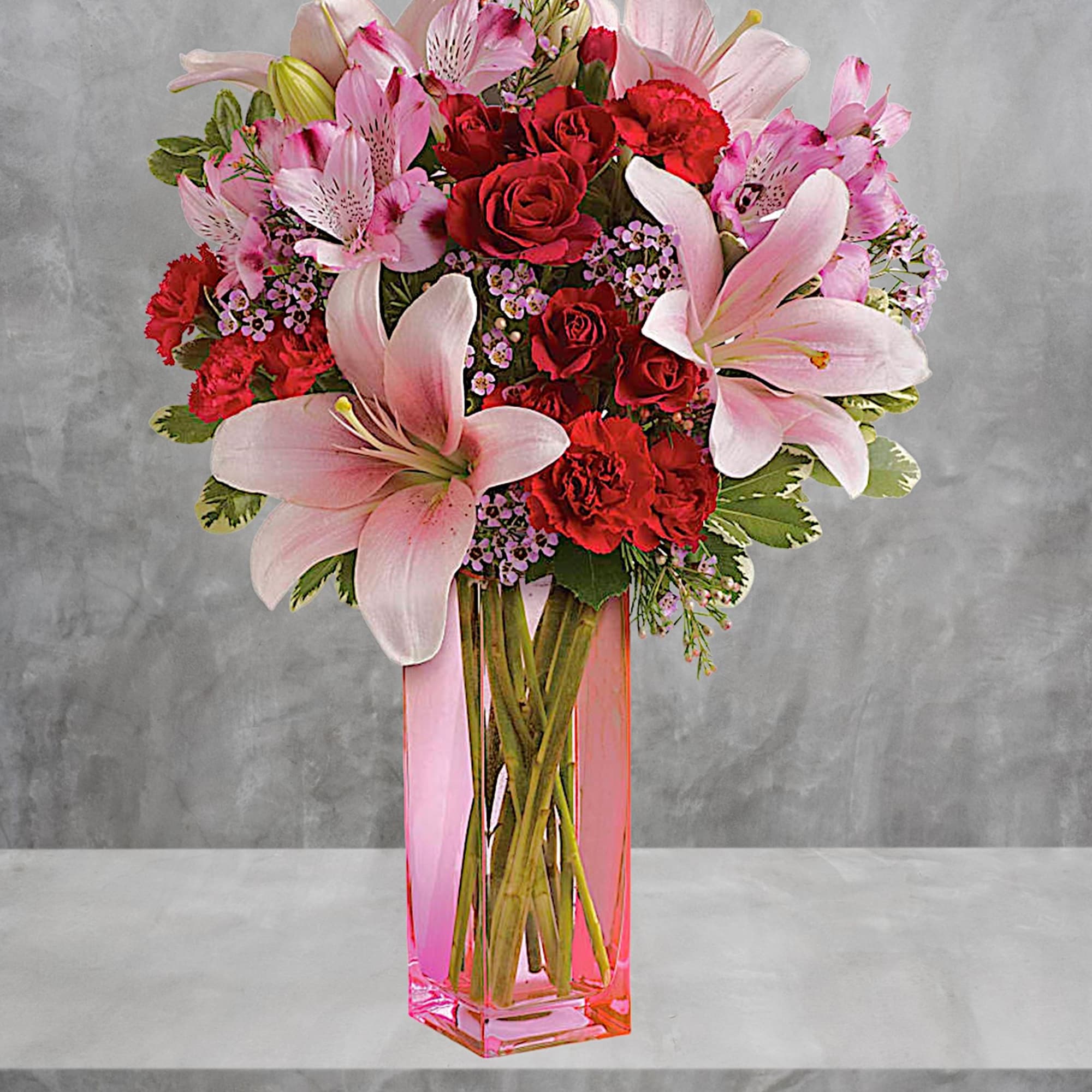 Pink lilies and red roses arranged in a tall pink vase
