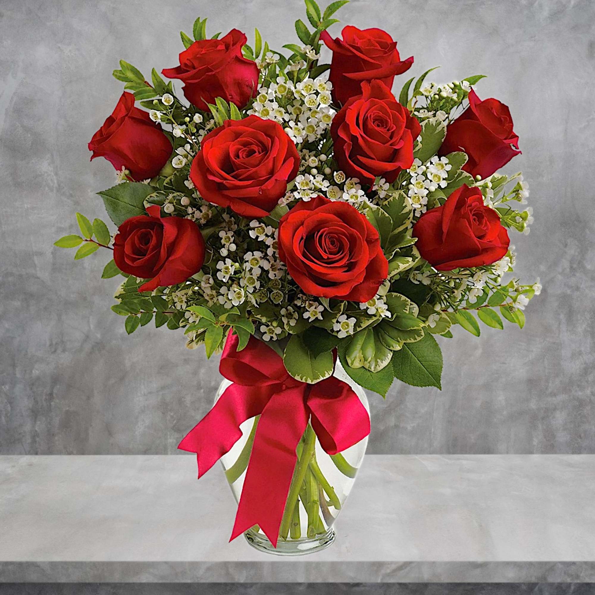 Red roses arranged in a clear glass vase with a pink ribbon