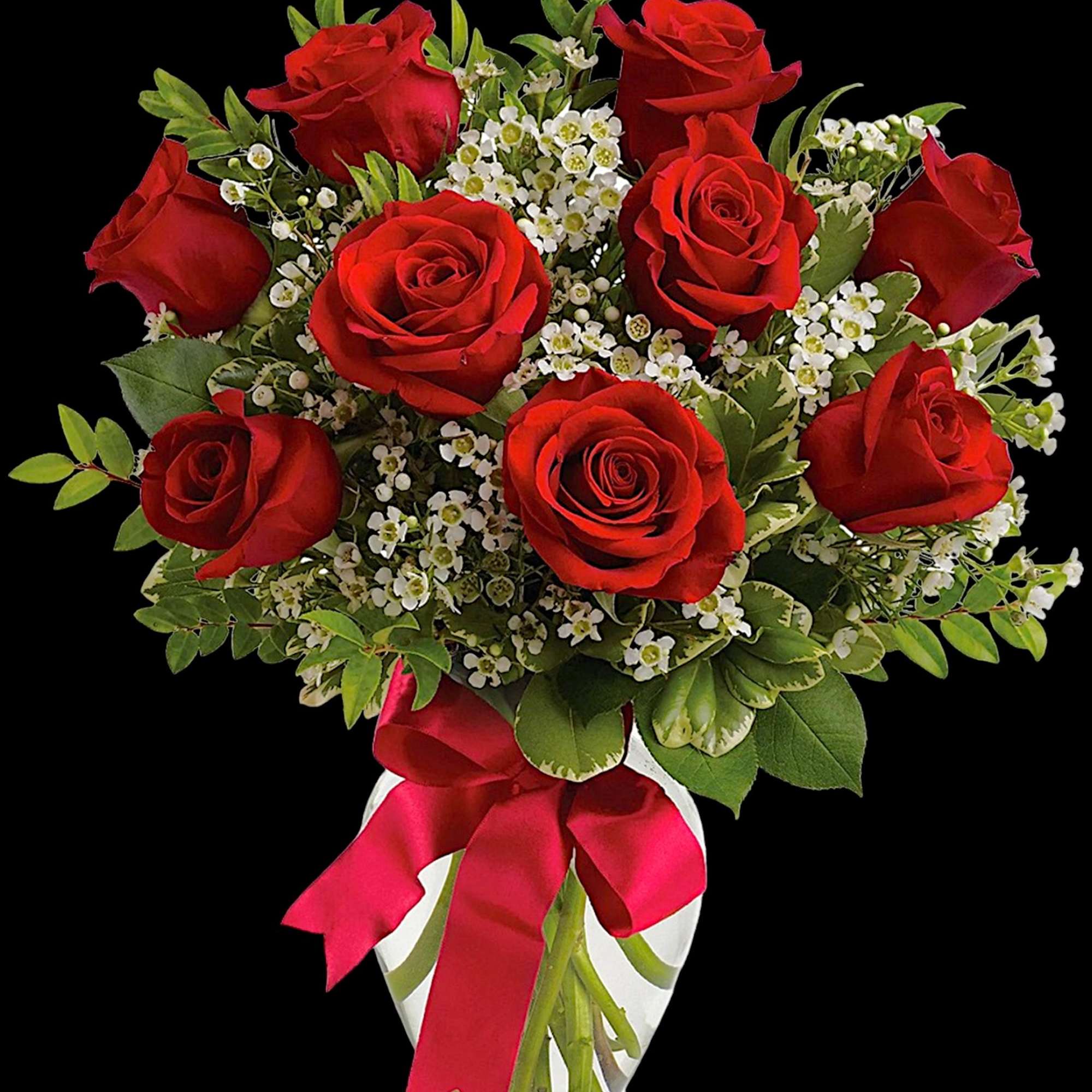 Red roses with white filler flowers in a clear vase tied with a pink ribbon