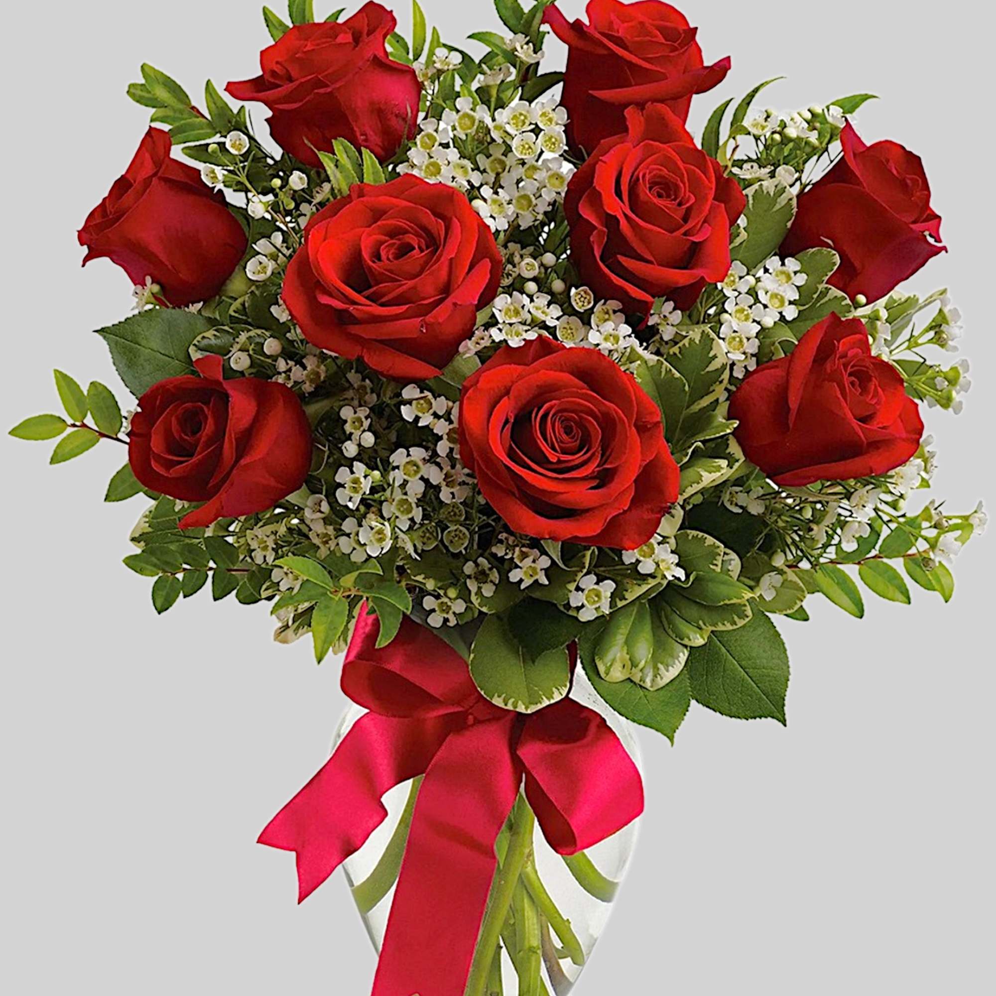 Bouquet of red roses with white filler flowers in a glass vase tied with a red ribbon