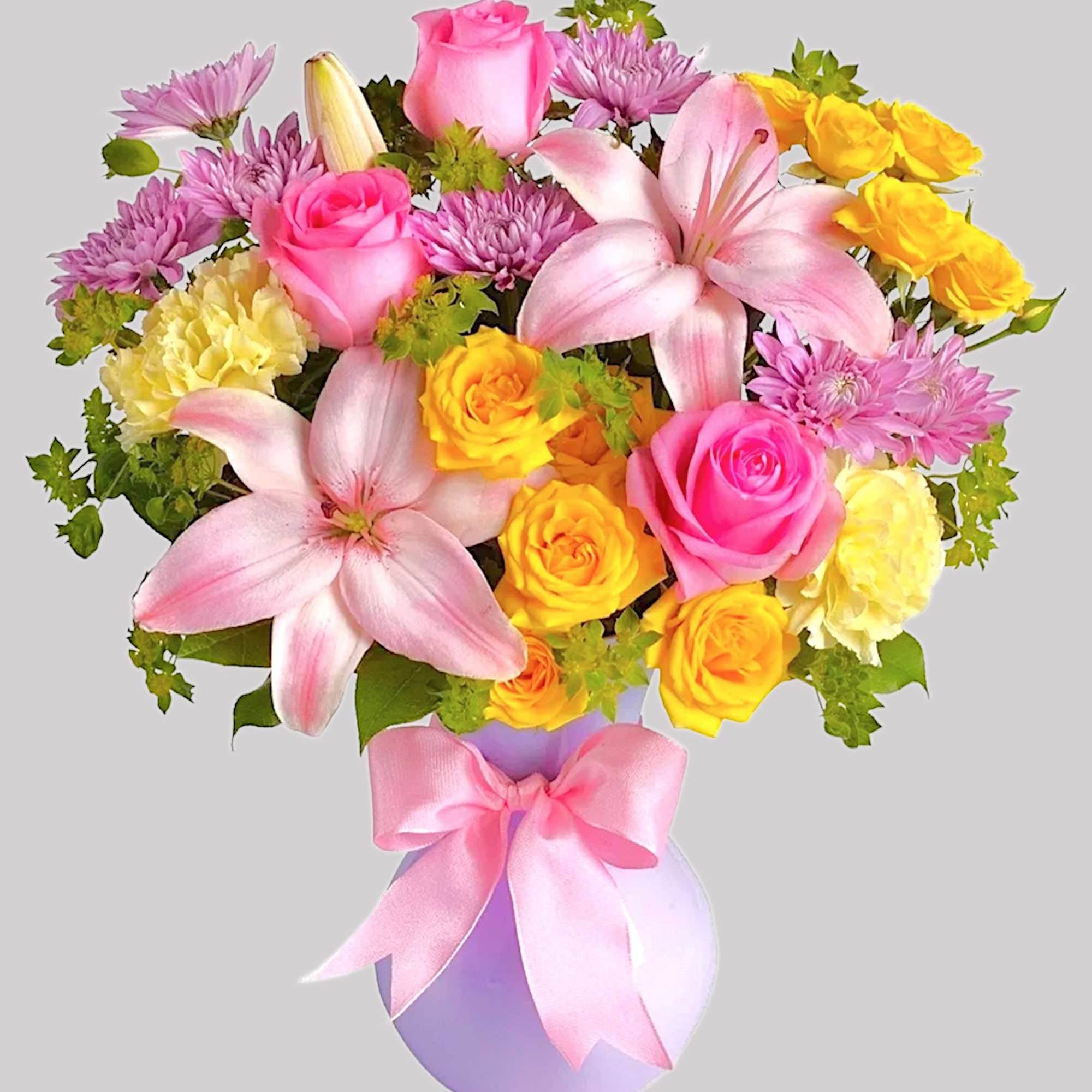 Bouquet of pink lilies, roses, and yellow carnations in a lavender vase with a pink bow