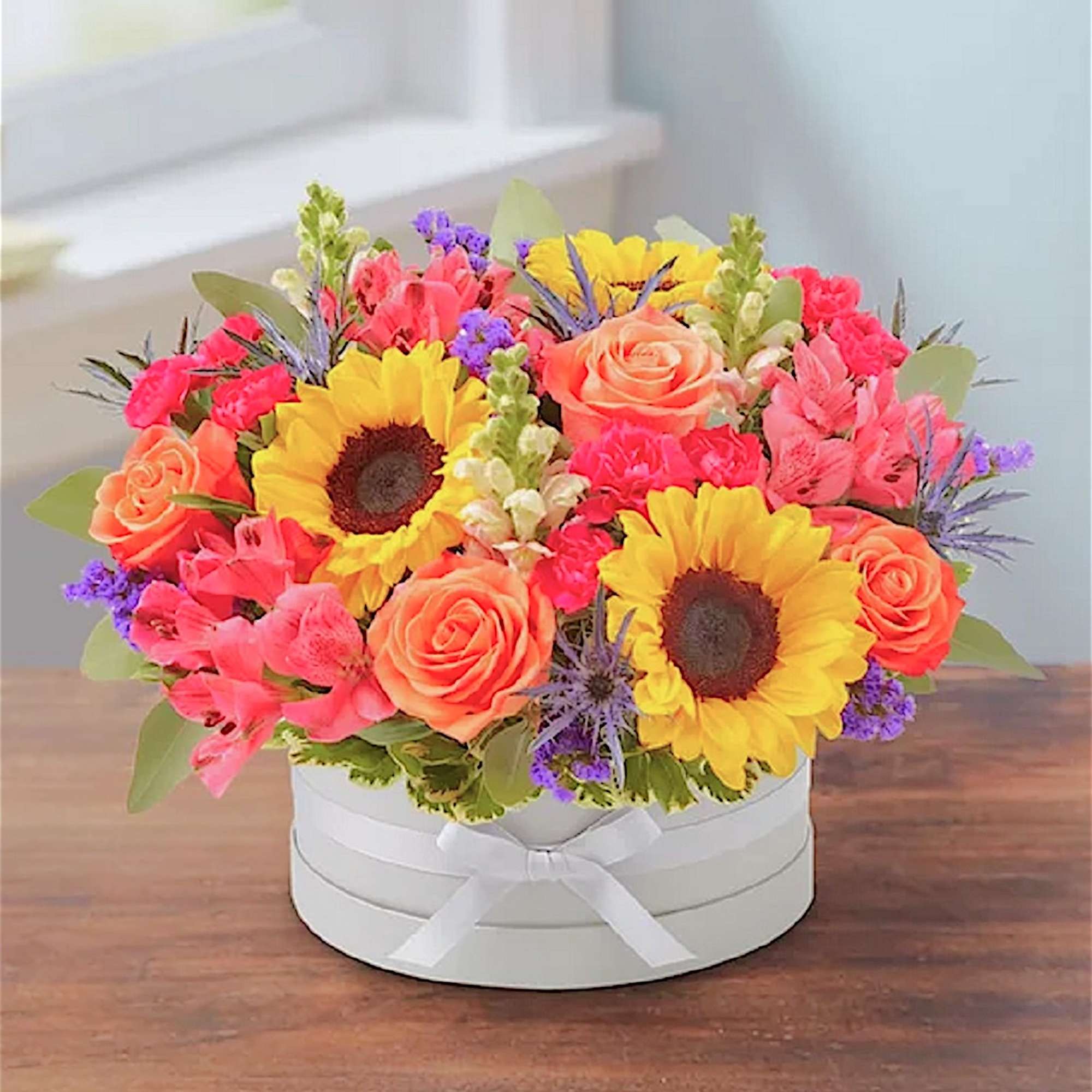 Bright bouquet of sunflowers, roses, and pink blooms in a white hat box