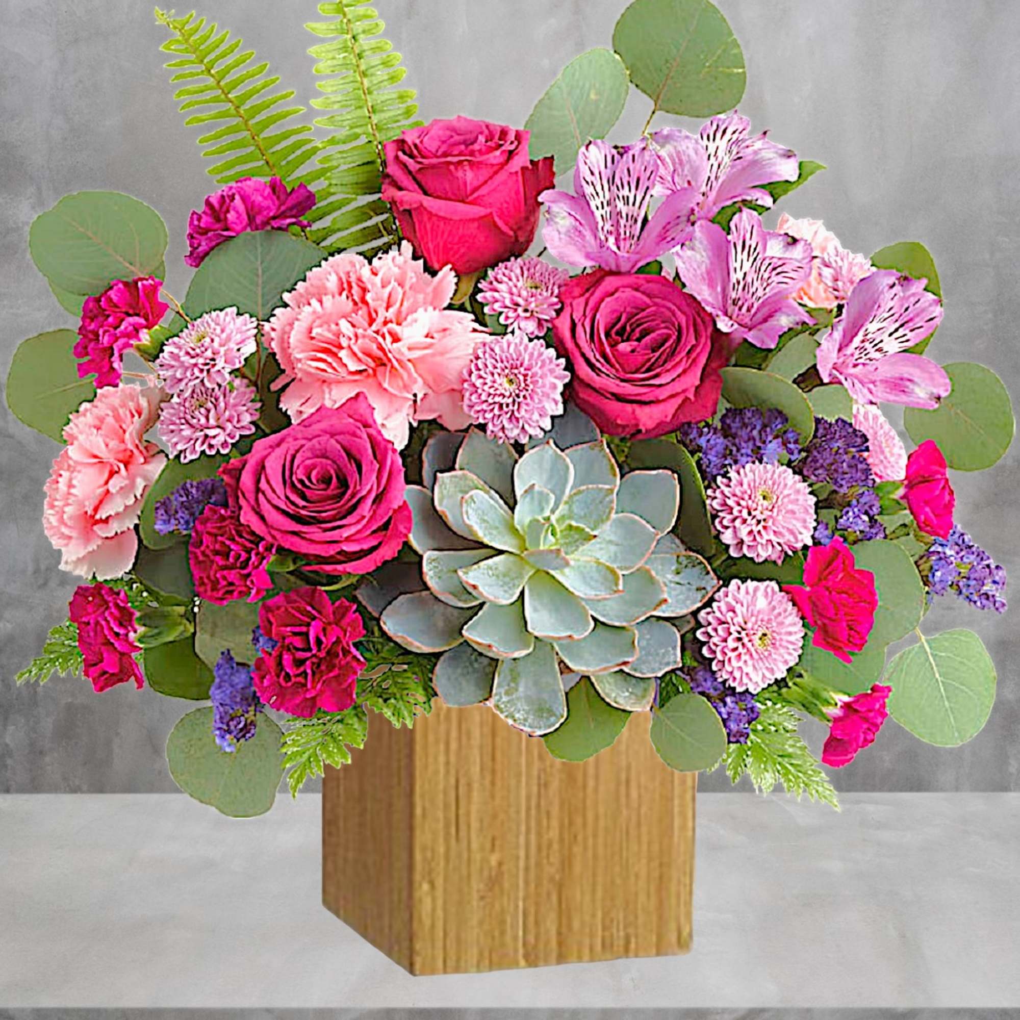 Pink roses and carnations arranged with a succulent in a wooden box.
