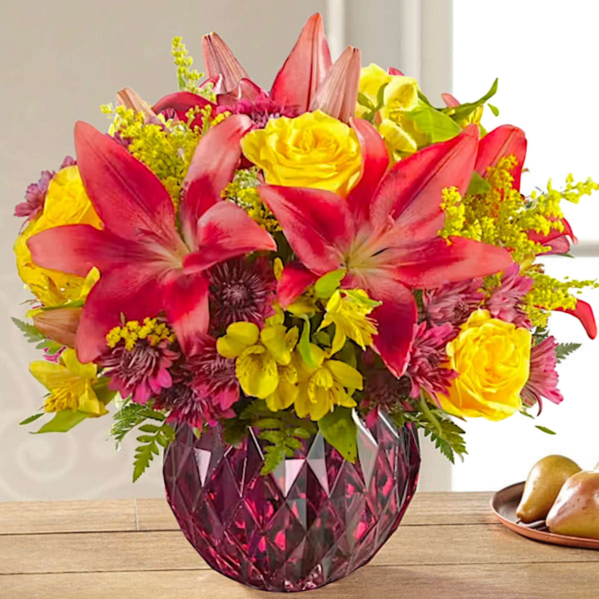 Bouquet of pink lilies, yellow roses, and mixed flowers in a pink glass vase