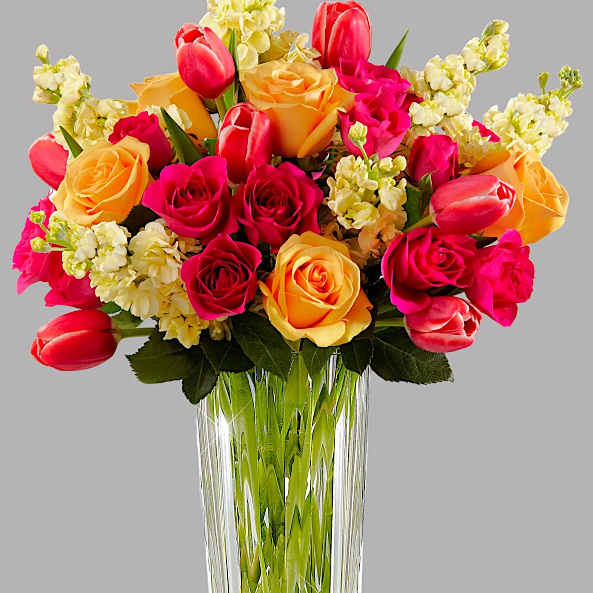 Bouquet of red, pink, and yellow roses with tulips in a clear glass vase